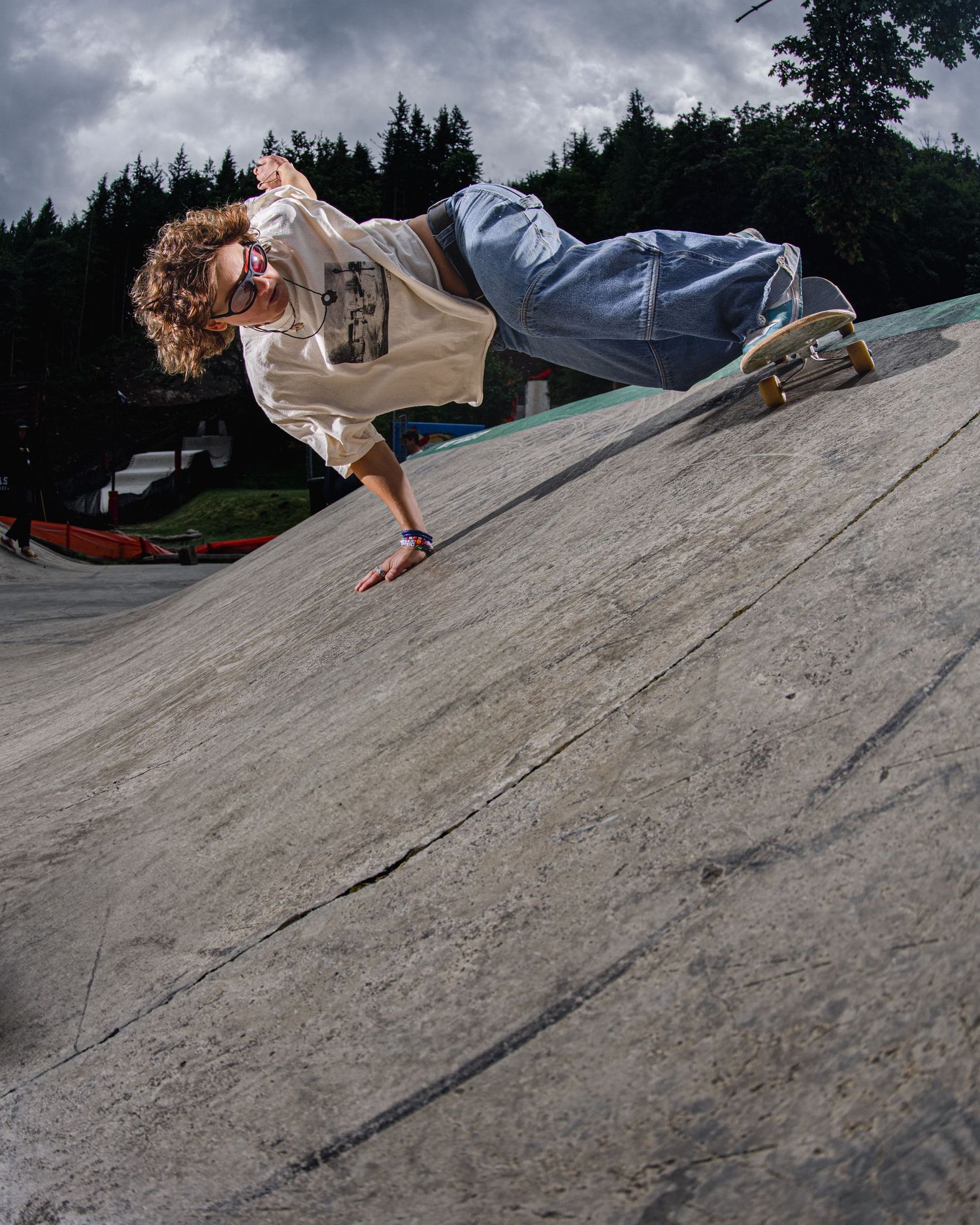 A skateboarder performs a creative handplant trick on a concrete slope with stormy skies overhead.