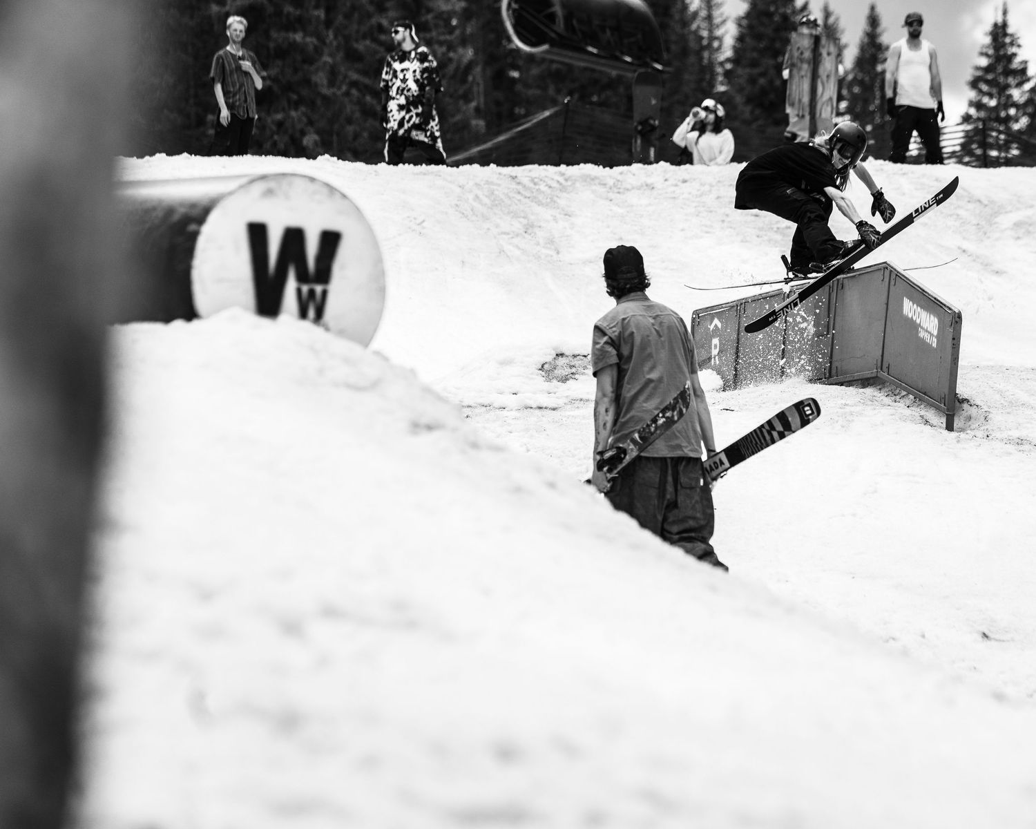 Snowboarders performing tricks on terrain park features with W logo visible in background.