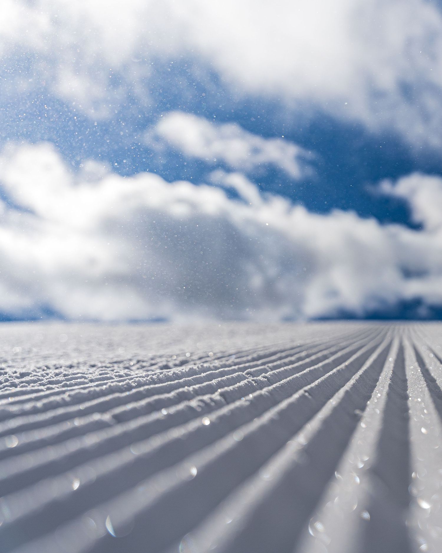 Close-up of freshly groomed snow with parallel lines under a cloudy blue sky.