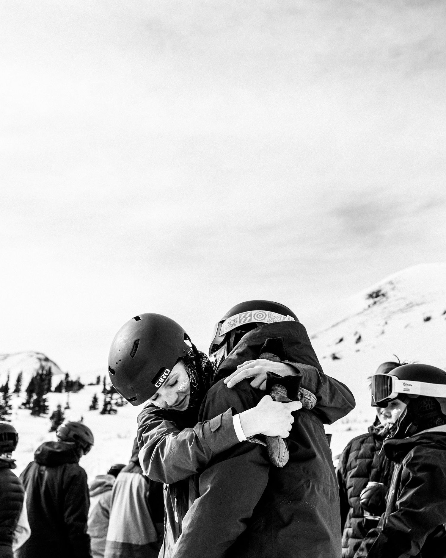 Group of skiers gather on snowy slope wearing winter gear and helmets.