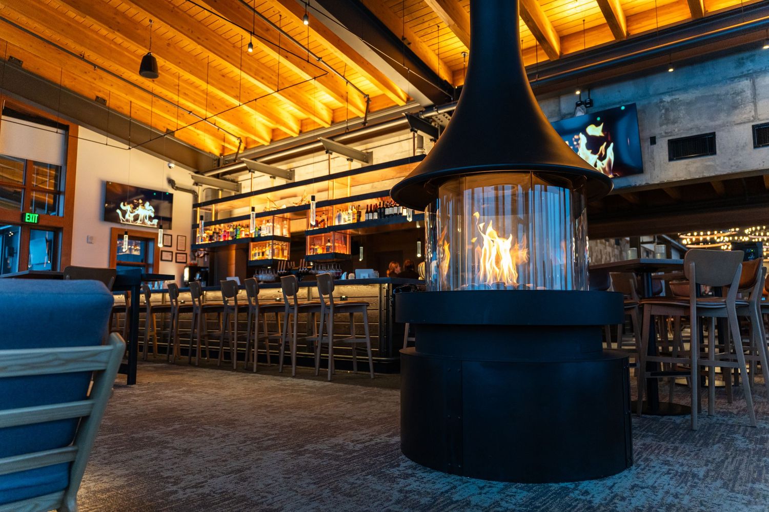 Modern restaurant interior with warm lighting and rustic wooden ceiling beams.
