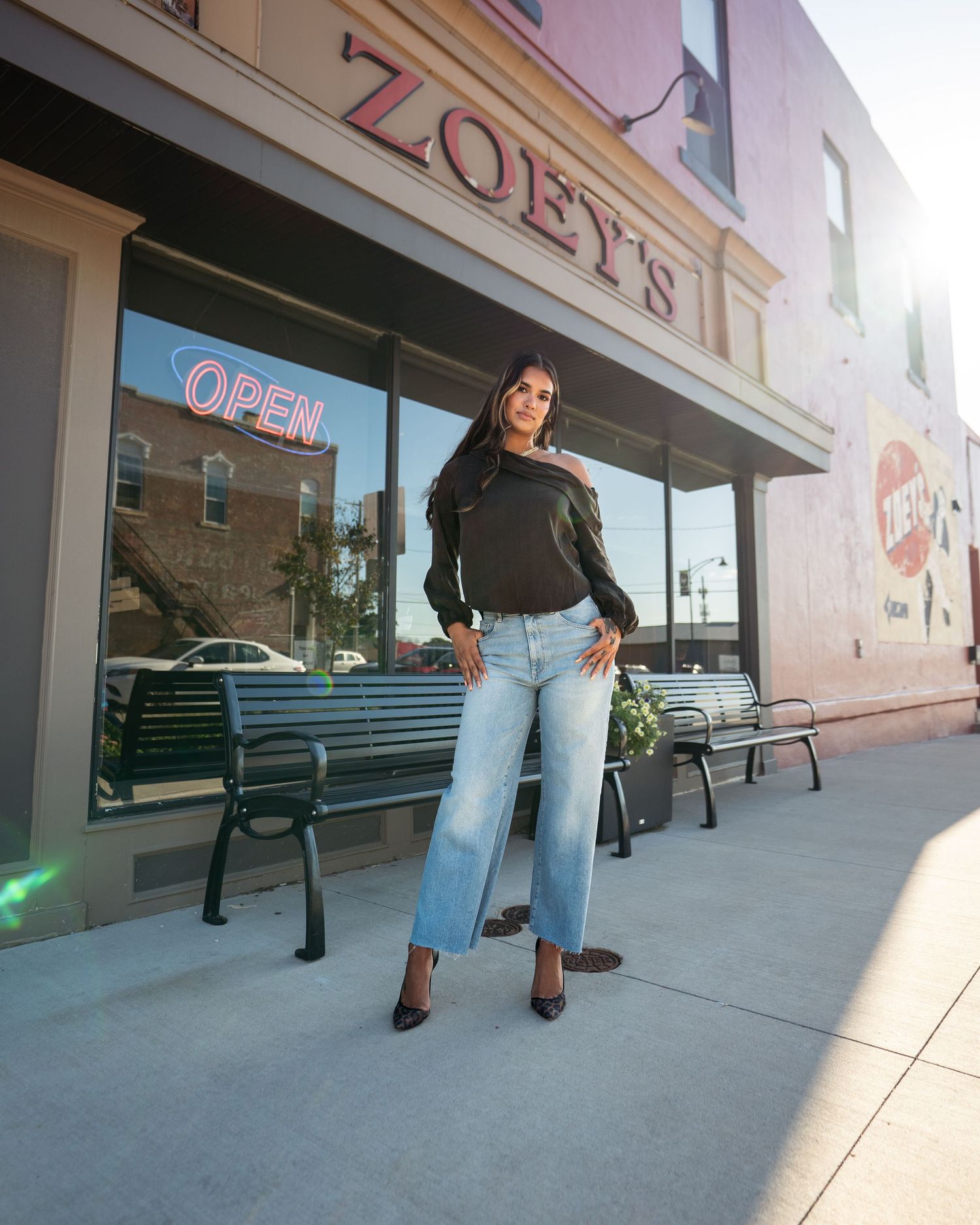 Casual streetwear outfit photographed in front of Zoey's storefront with benches and neon open sign.