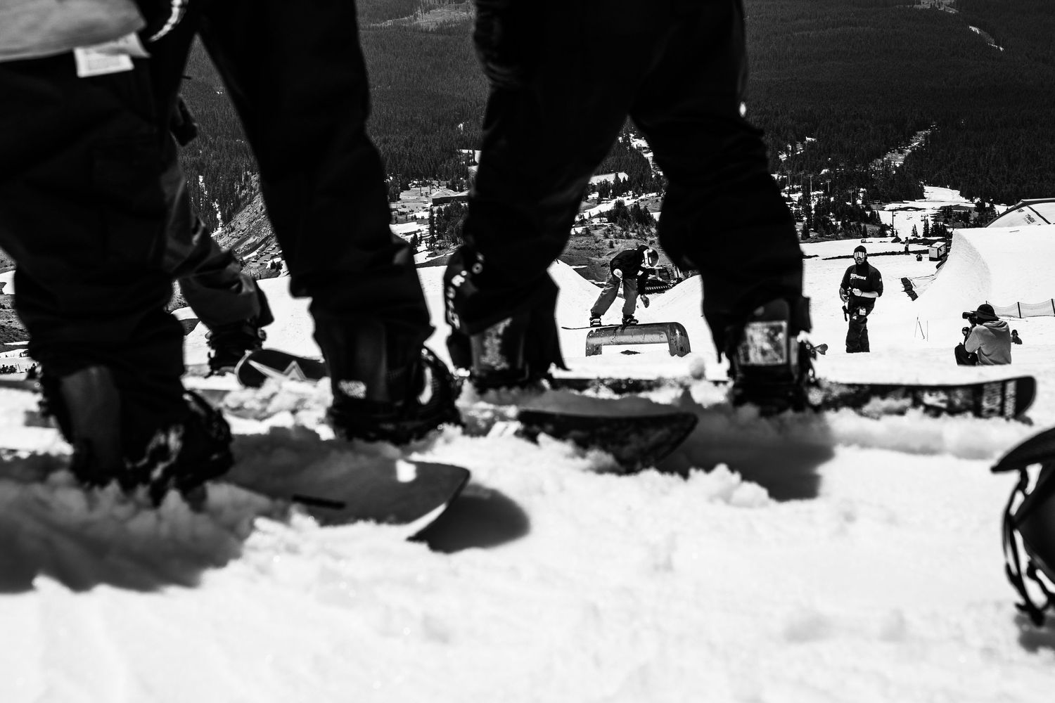 Low angle black and white shot of snowboarders' boots on snowy ground.