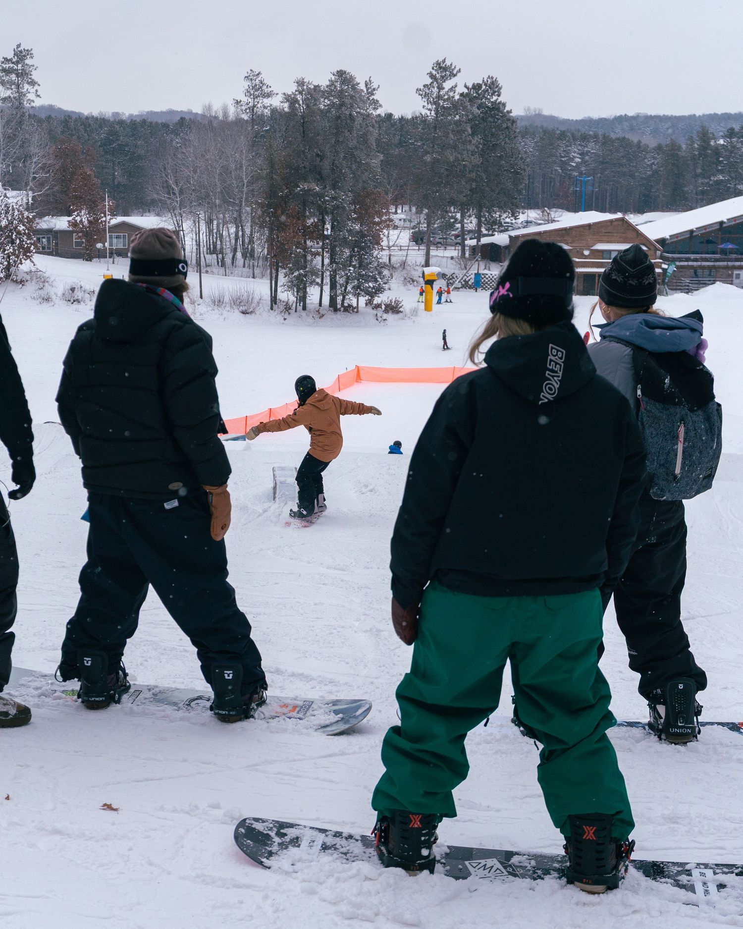 Group of snowboarders watching a rider perform tricks on a snowy slope at a winter ski resort.