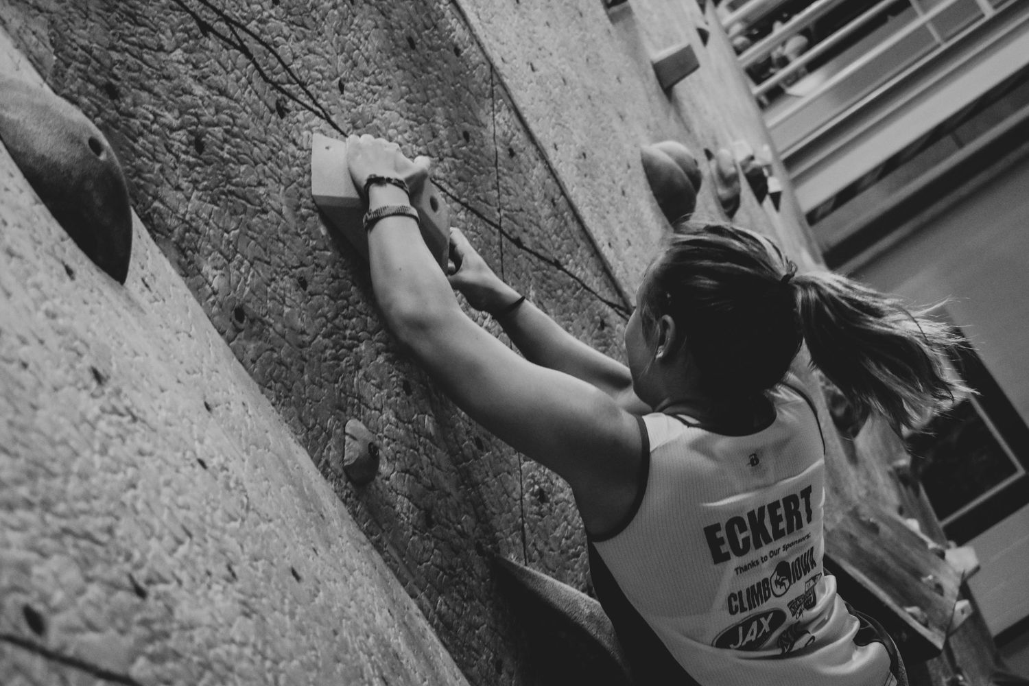 Indoor climber wearing an Eckert tank top carefully positions hands on climbing wall holds.