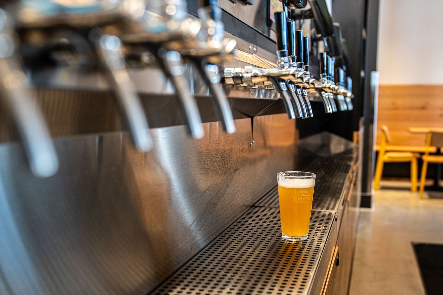 Draft beer tap system with a single glass of golden beer on black metal bar counter.