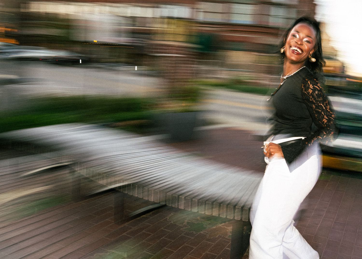 Motion blur photo of someone spinning joyfully in white pants and black top against an urban background.