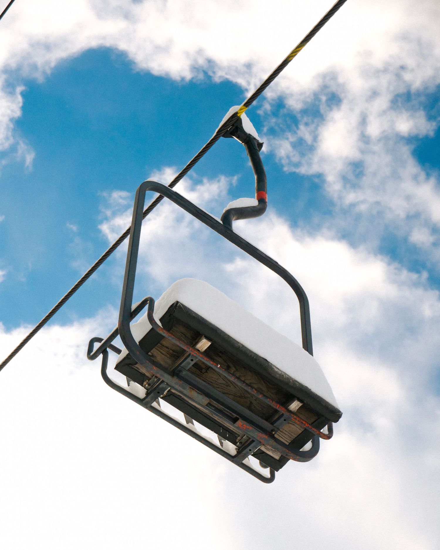 Empty ski lift chair photographed from below against blue sky and white clouds.