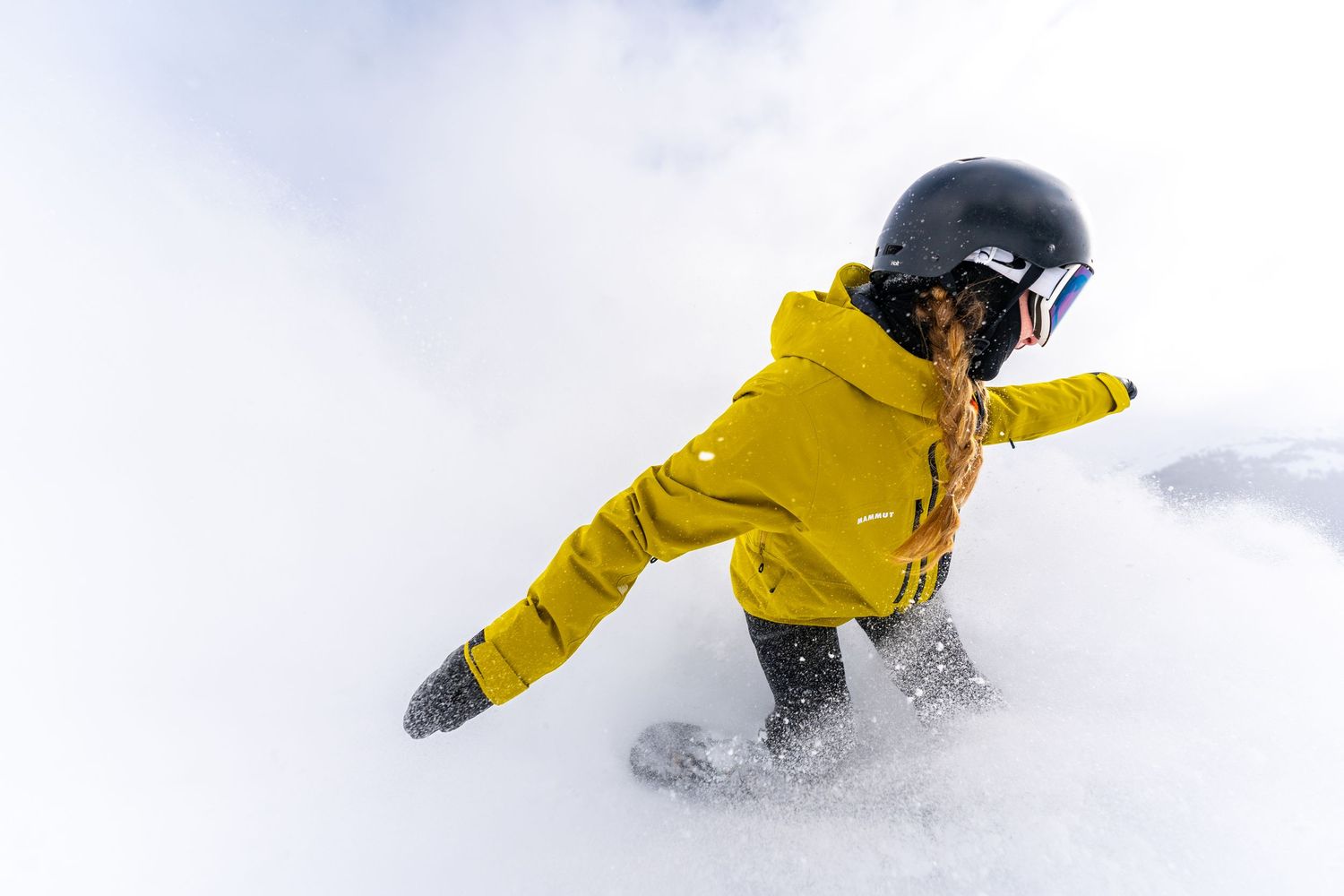 Action shot of snowboarder in bright yellow jacket carving through fresh powder snow.