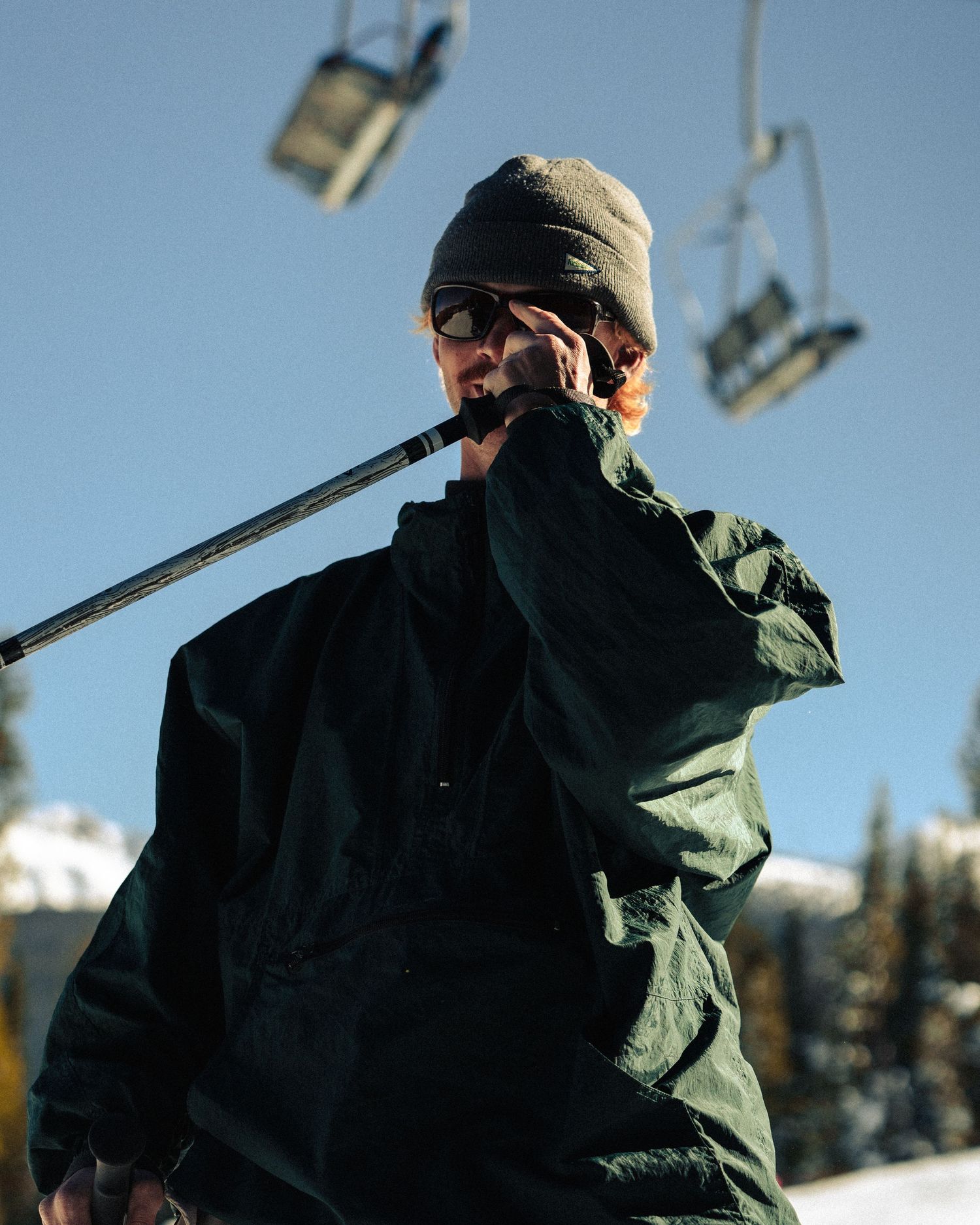 Skier in winter gear holding ski poles against blue sky with chairlifts in background.
