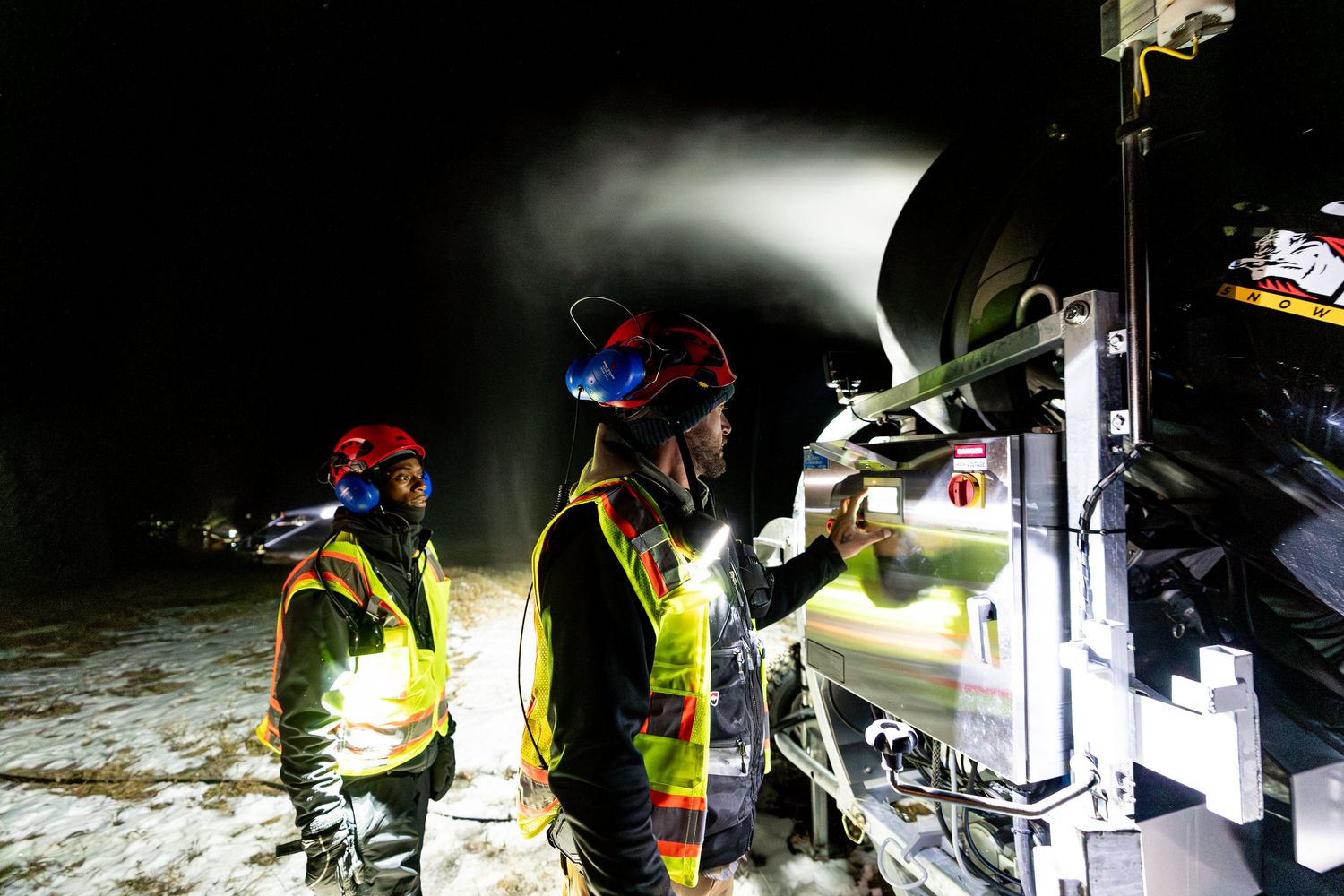 Ski resort workers operate snow-making equipment controls during nighttime operations.