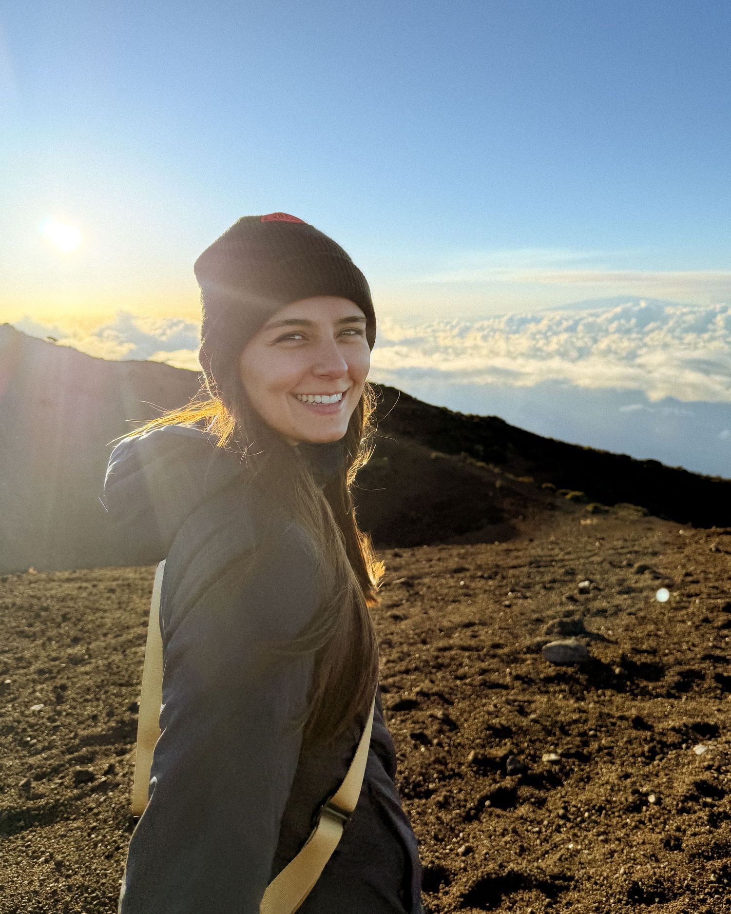 Hiker enjoying the scenic view above the clouds at sunrise on a mountain summit trail.