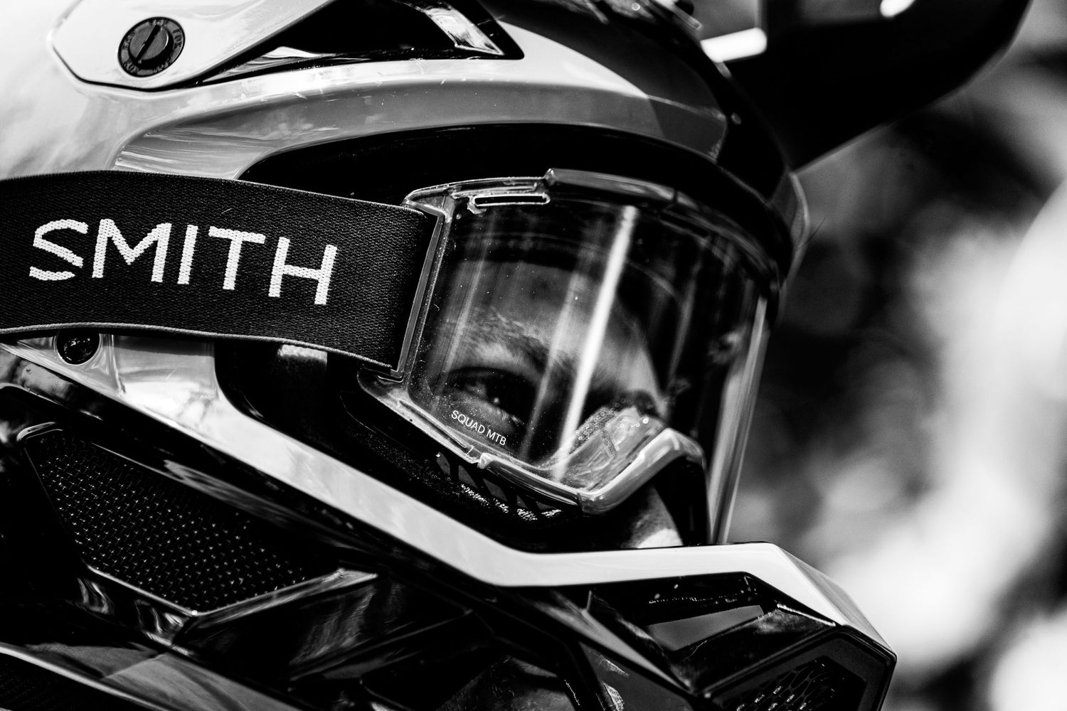 Close-up black and white detail of Smith racing goggles and helmet gear against blurred background.