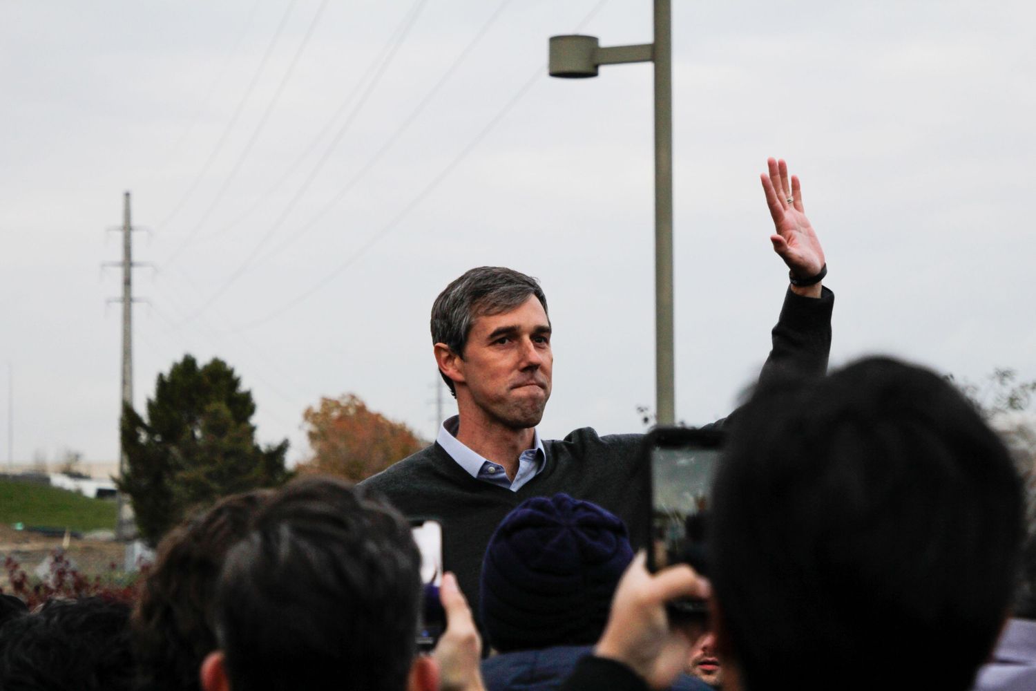 Person gestures to a crowd gathered at an outdoor public event during daytime.