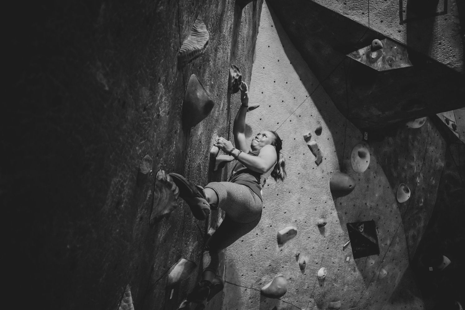 Climber scaling an indoor climbing wall with focused determination in monochrome.