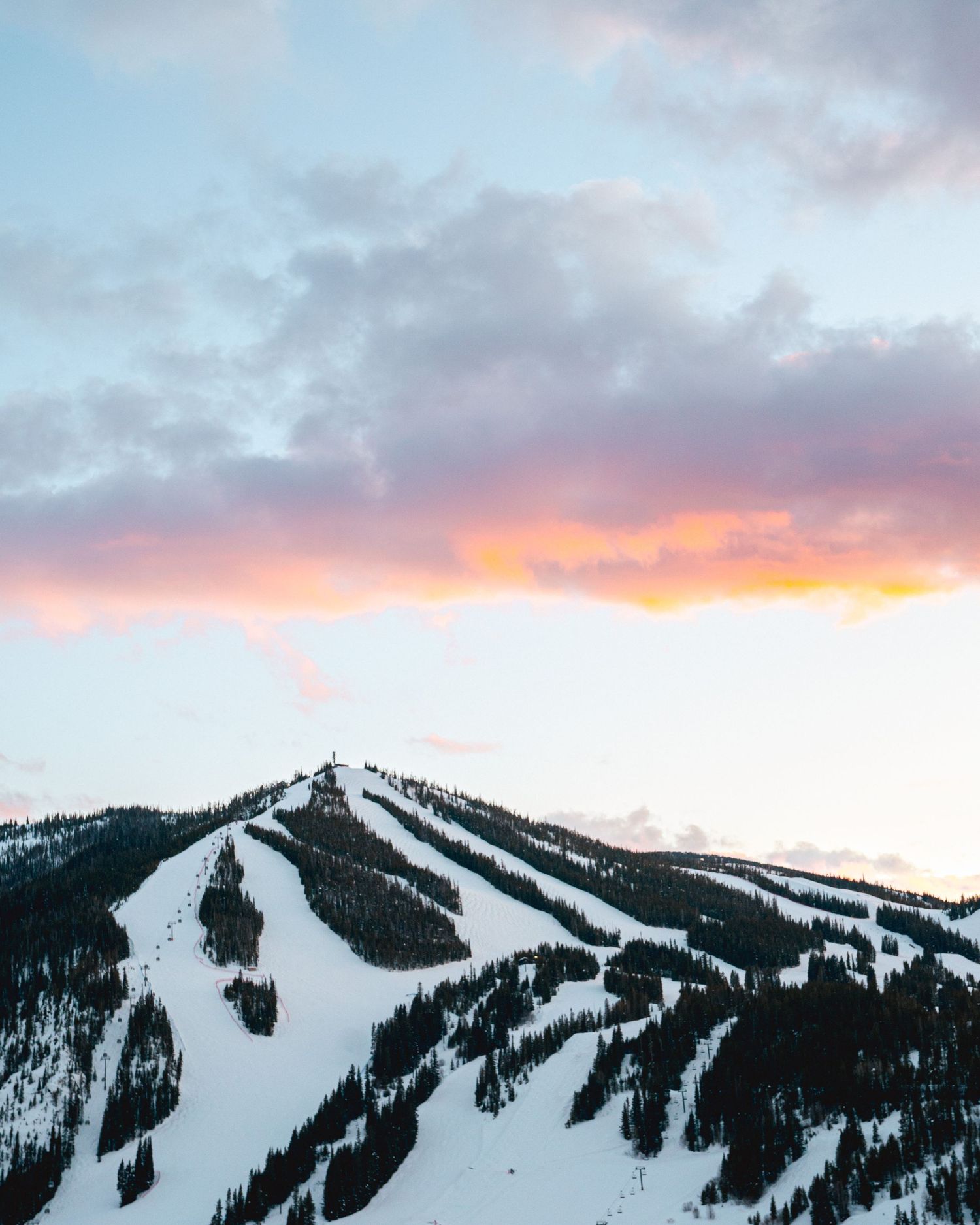 Snow-covered ski slopes on a mountain with pink and purple sunset clouds.