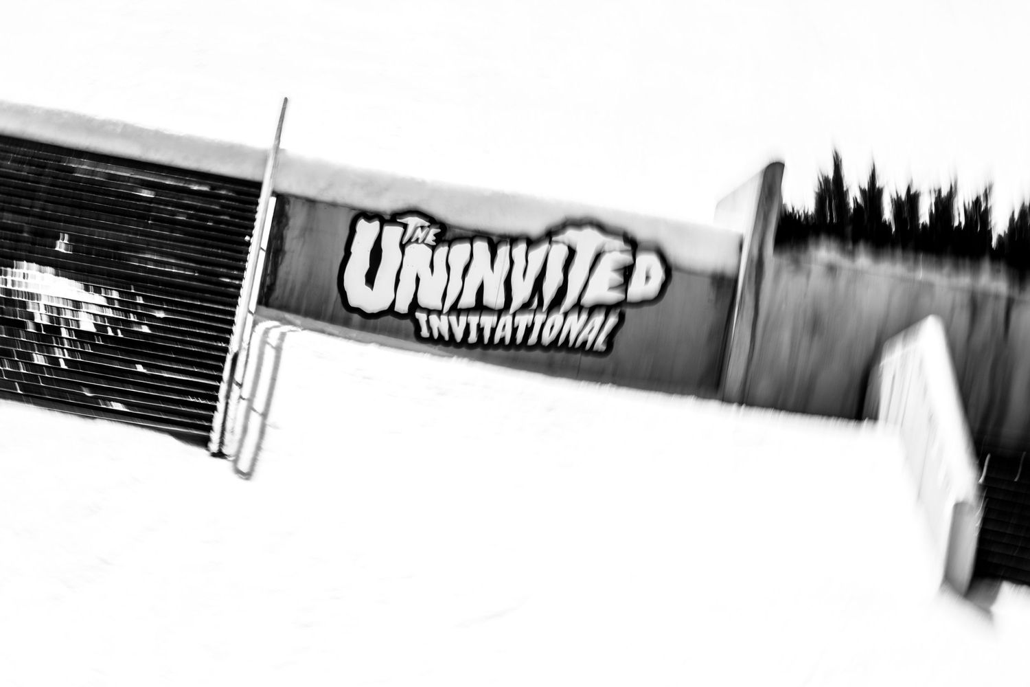 Black and white photo of The Uninvited Invitational skateboarding event banner on a rail.