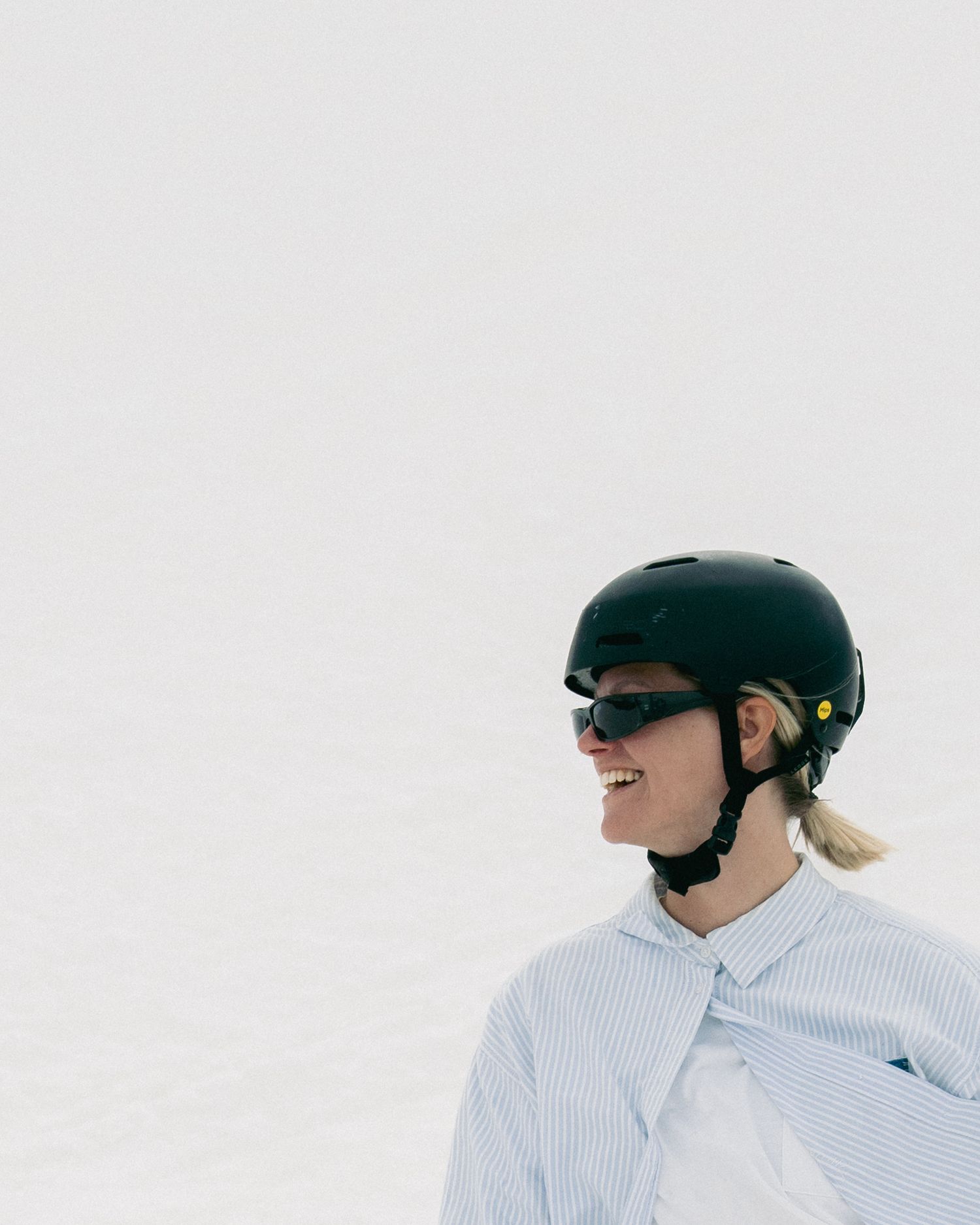 Smiling snowboarder wearing a black helmet and goggles on a snowy slope.