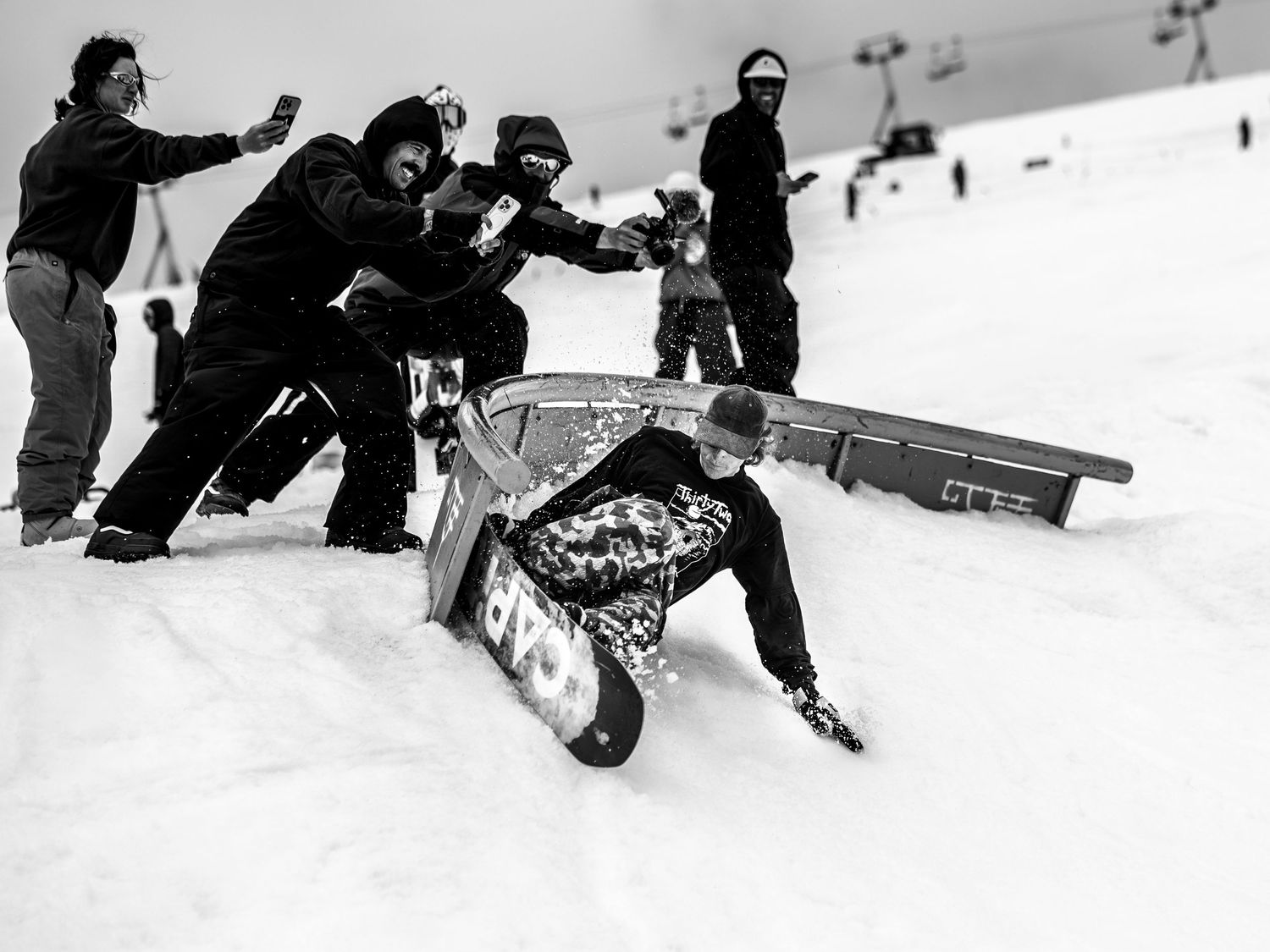 Group of snowboarders helping someone who took a tumble on snowy slope in black and white photo.