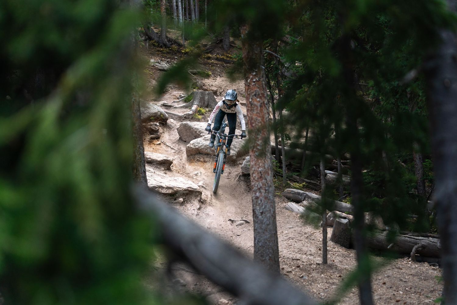 Mountain biker descending through dense forest on technical rocky single track.