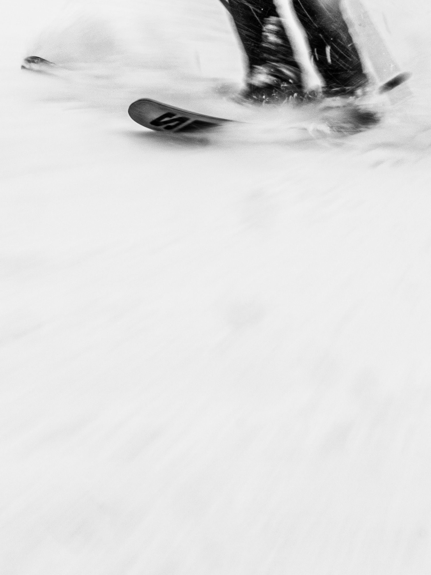 Abstract black and white close-up of skis gliding through fresh snow.
