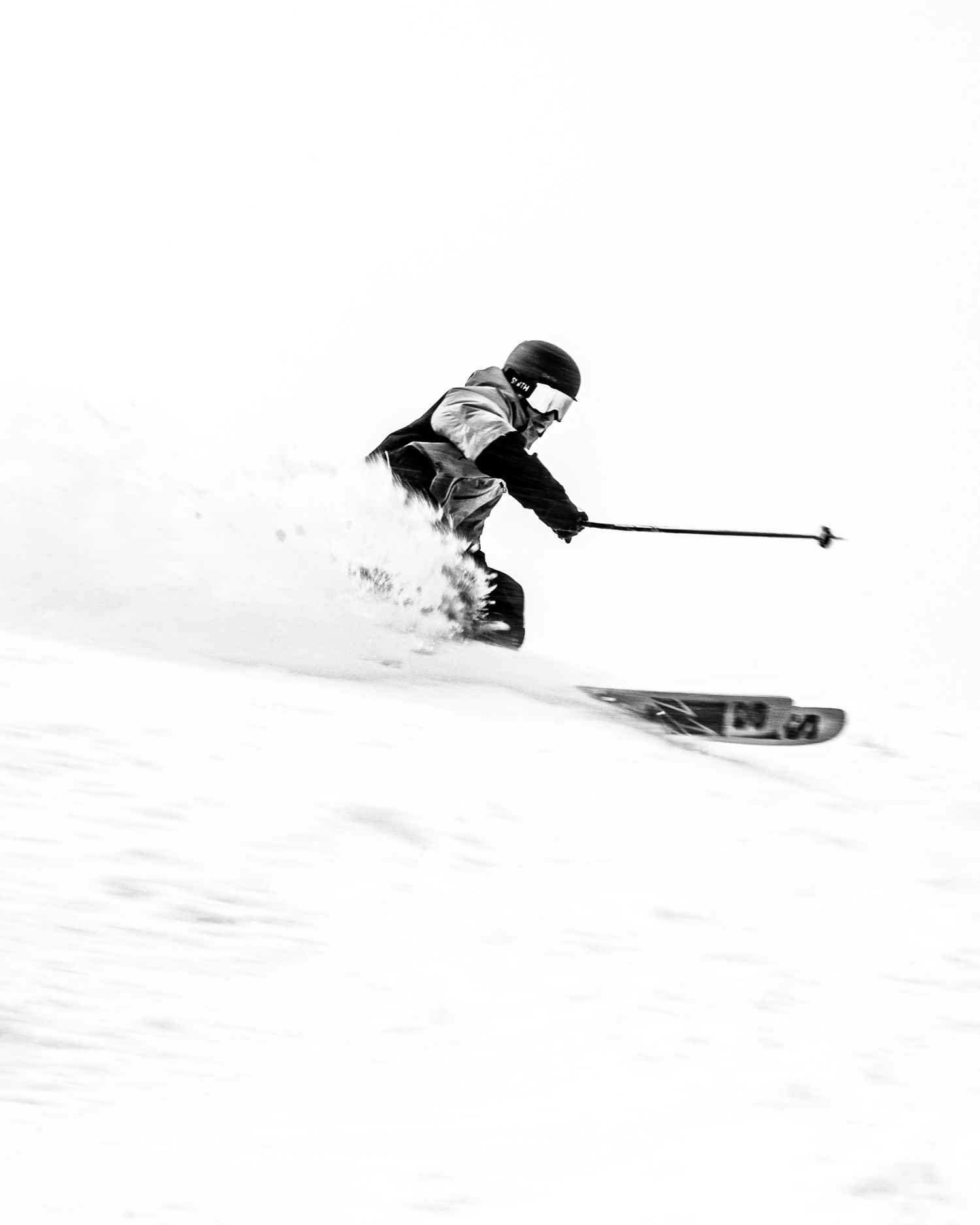 Black and white action shot of skier carving through fresh powder snow.