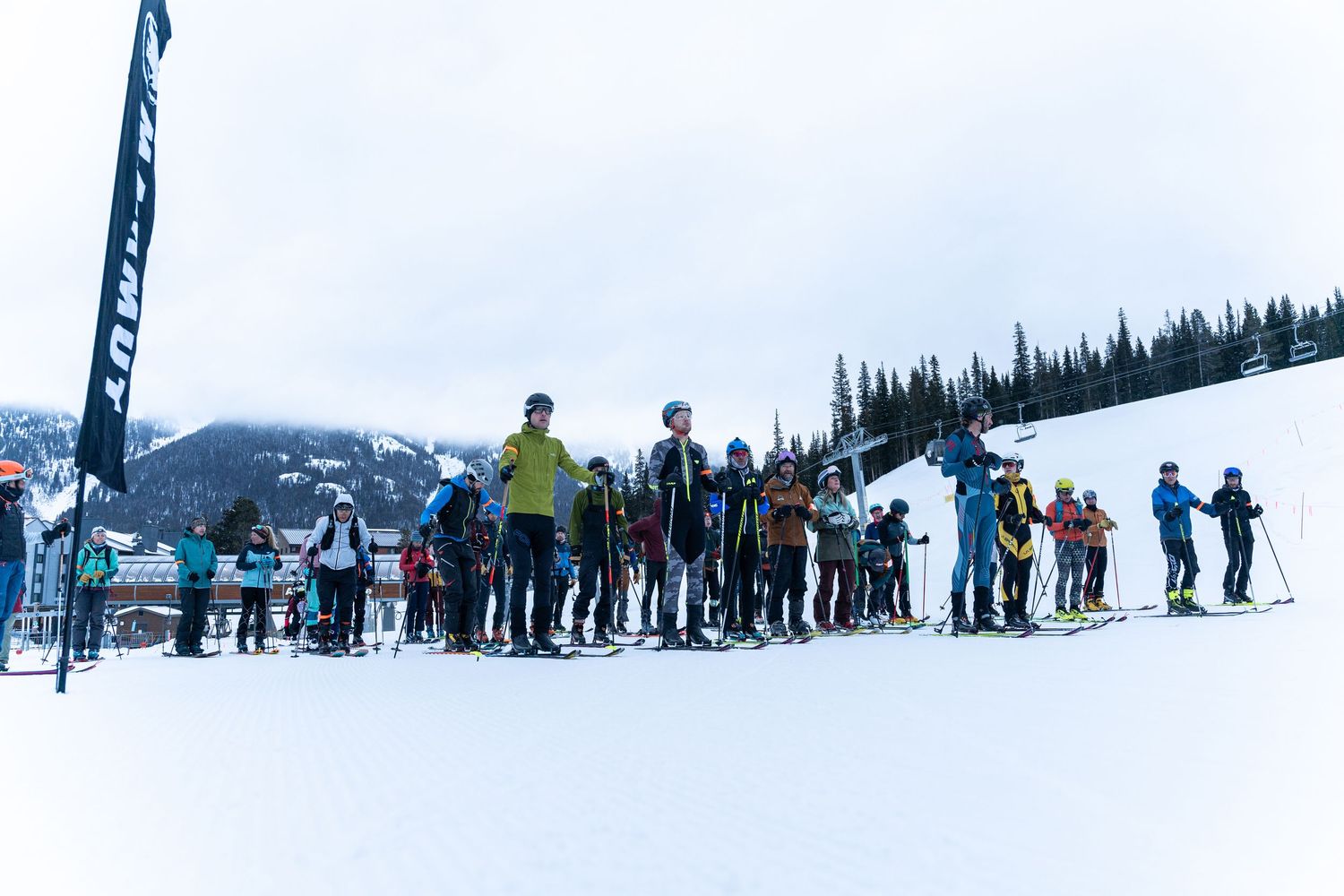 A line of skiers gather at the base of a snow-covered mountain slope during winter.