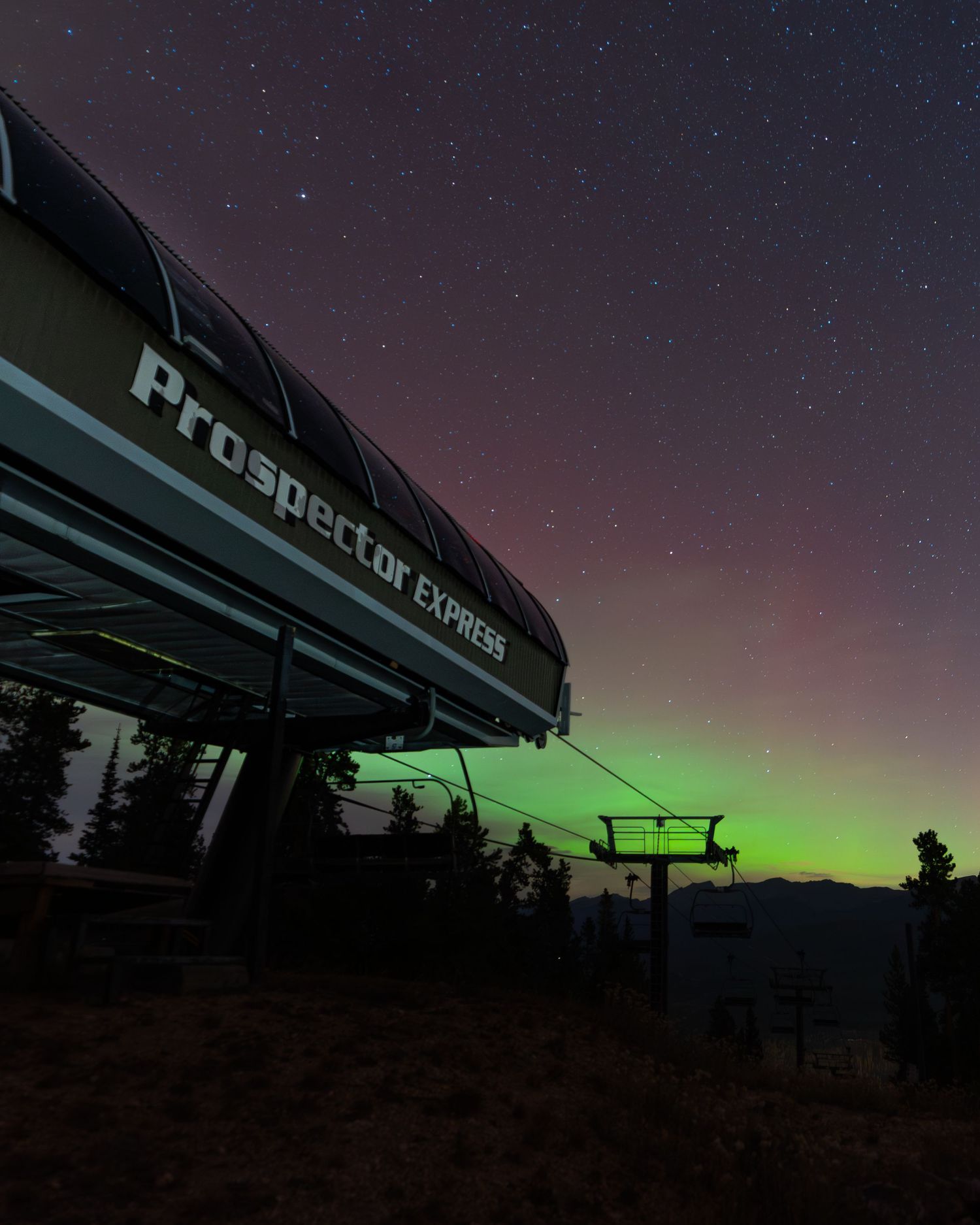 Ski lift silhouetted against the northern lights displaying vibrant green aurora in the night sky.
