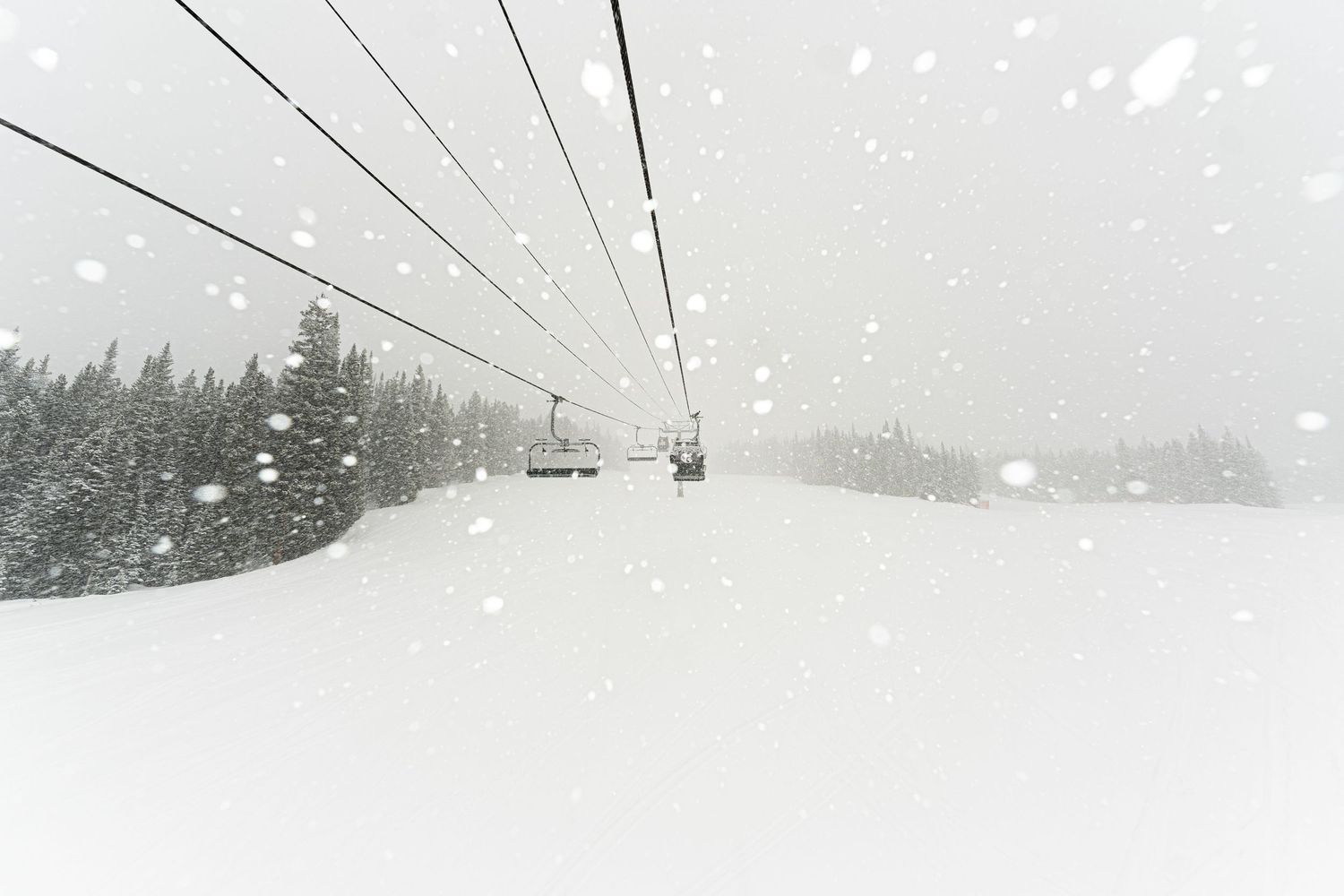 Ski lift cables stretch into foggy distance during heavy snowfall.