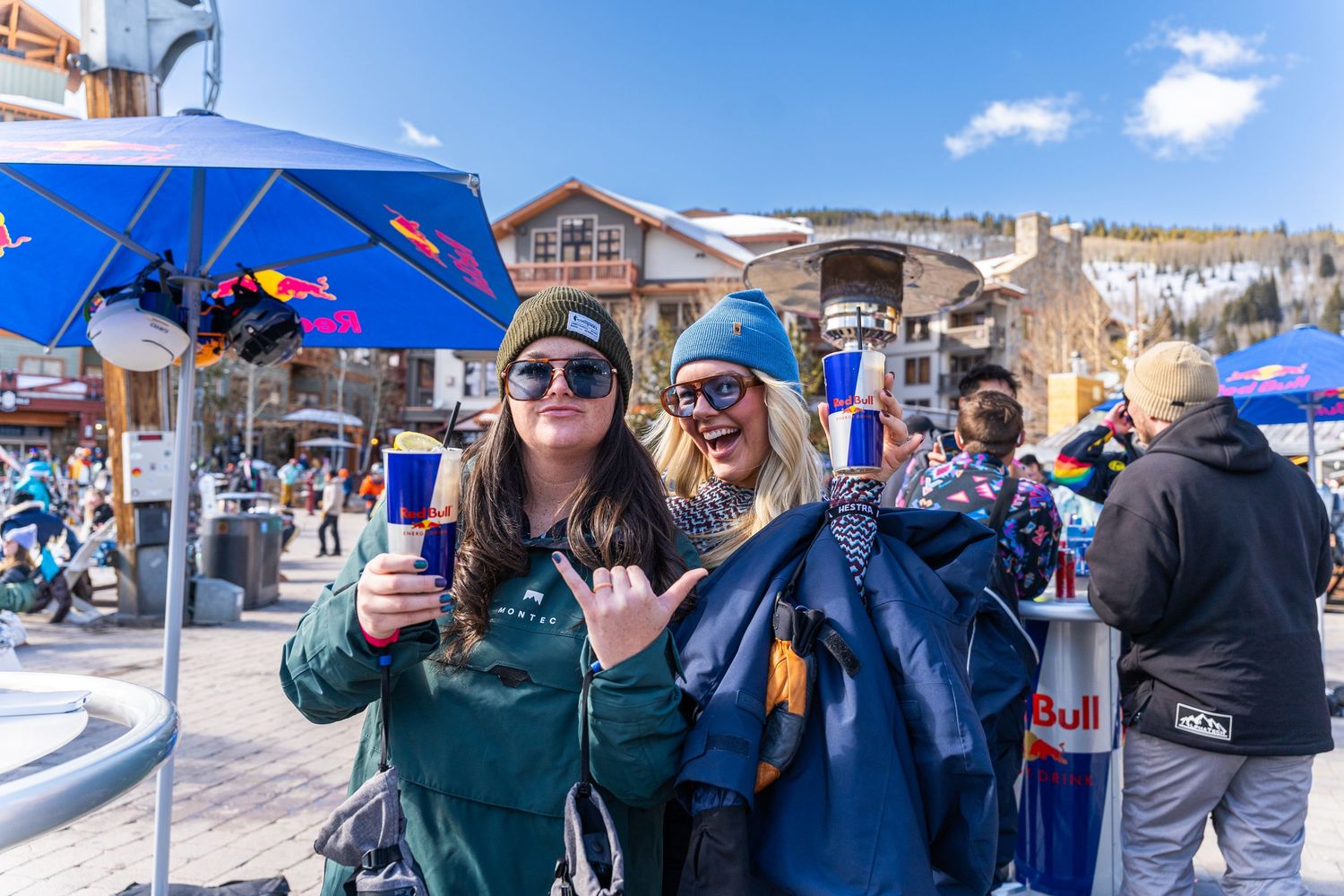 Friends enjoying beverages at a ski resort patio on a sunny winter day.