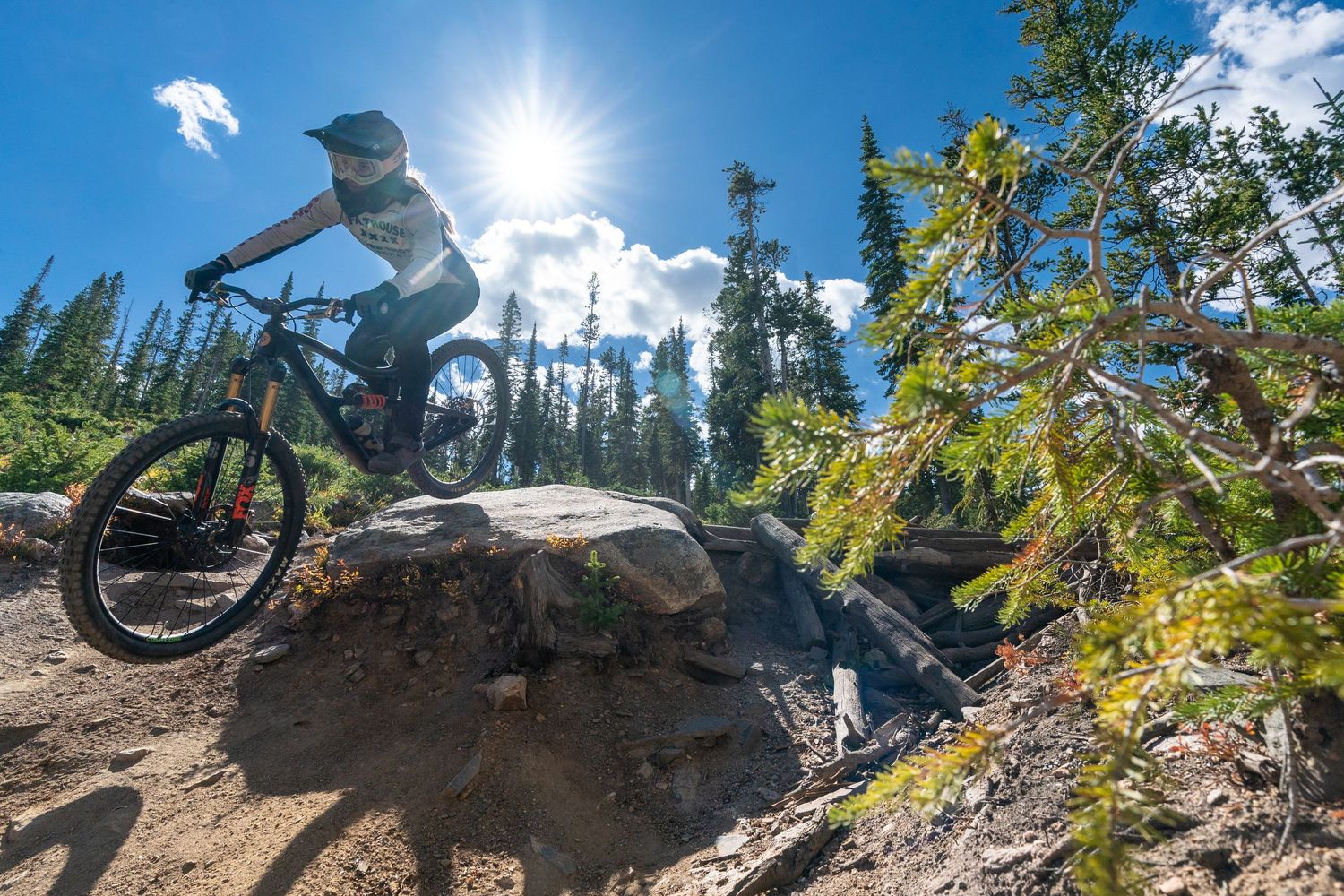 Mountain biker launches off rocky terrain with bright sunburst in background.