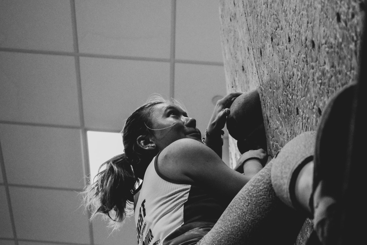 Indoor rock climber reaches upward while ascending steep climbing wall.
