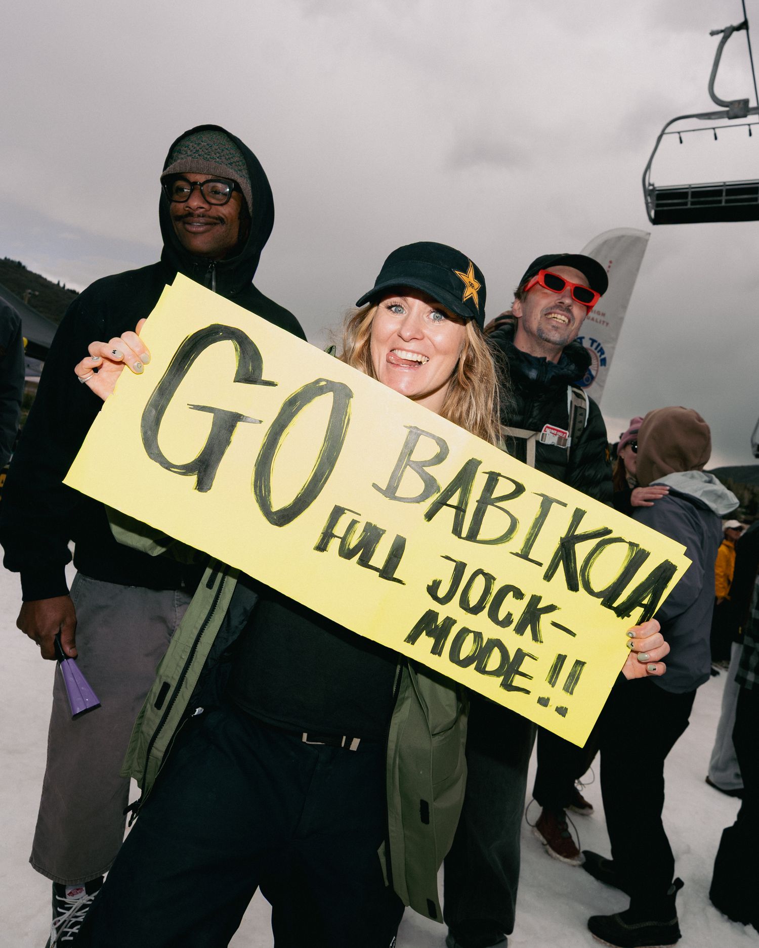 Excited fan holds yellow sign reading Go Babikoia Full Jock Mode at ski resort event.