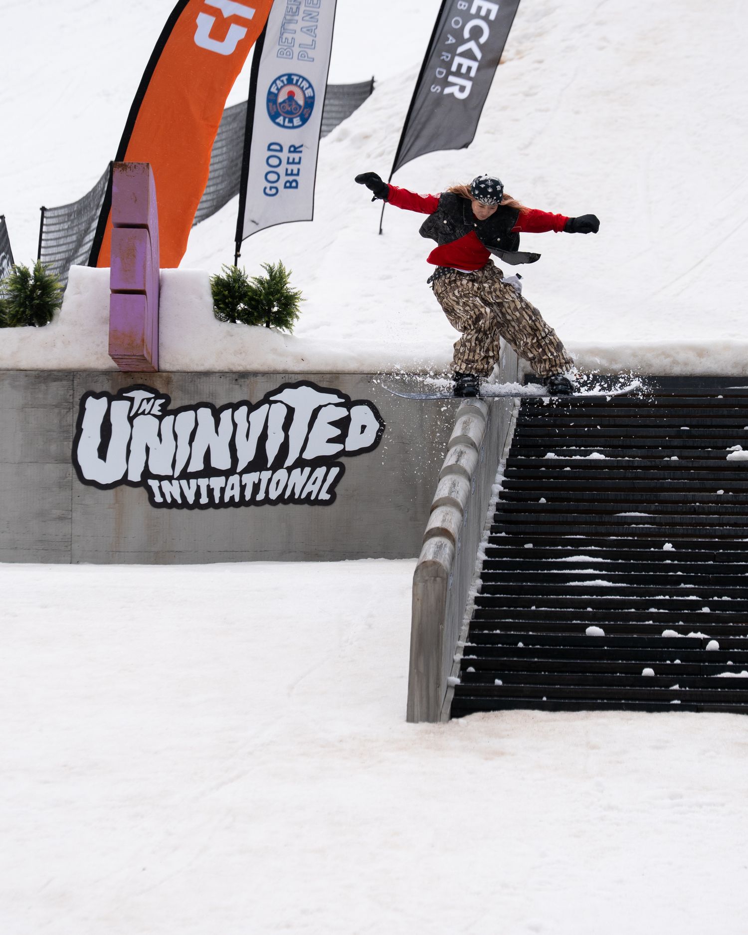 Snowboarder performs a rail grind trick at The Uninvited Invitational competition on a snowy mountain terrain park.