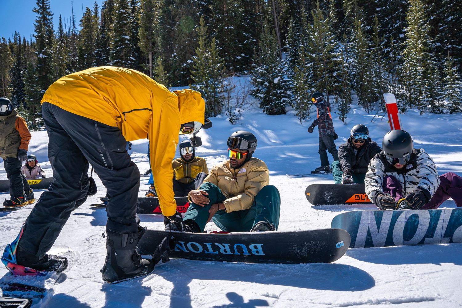 Snowboarding instructor helping student with equipment on snowy mountain slope.