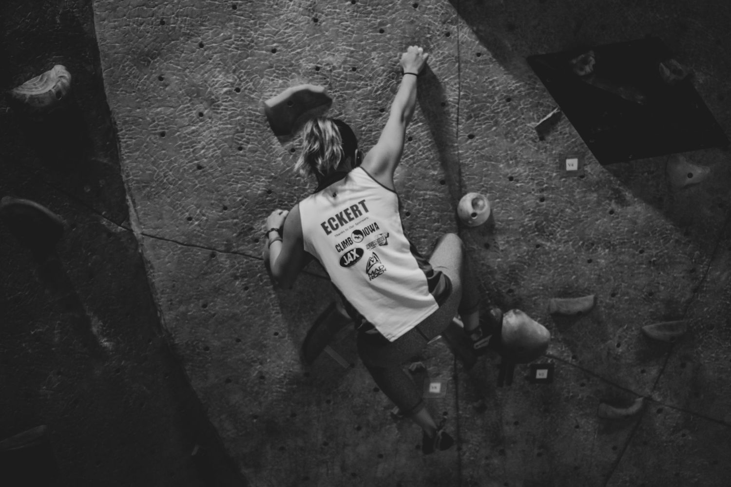 Rock climber reaching for next hold on indoor climbing wall in dramatic black and white.