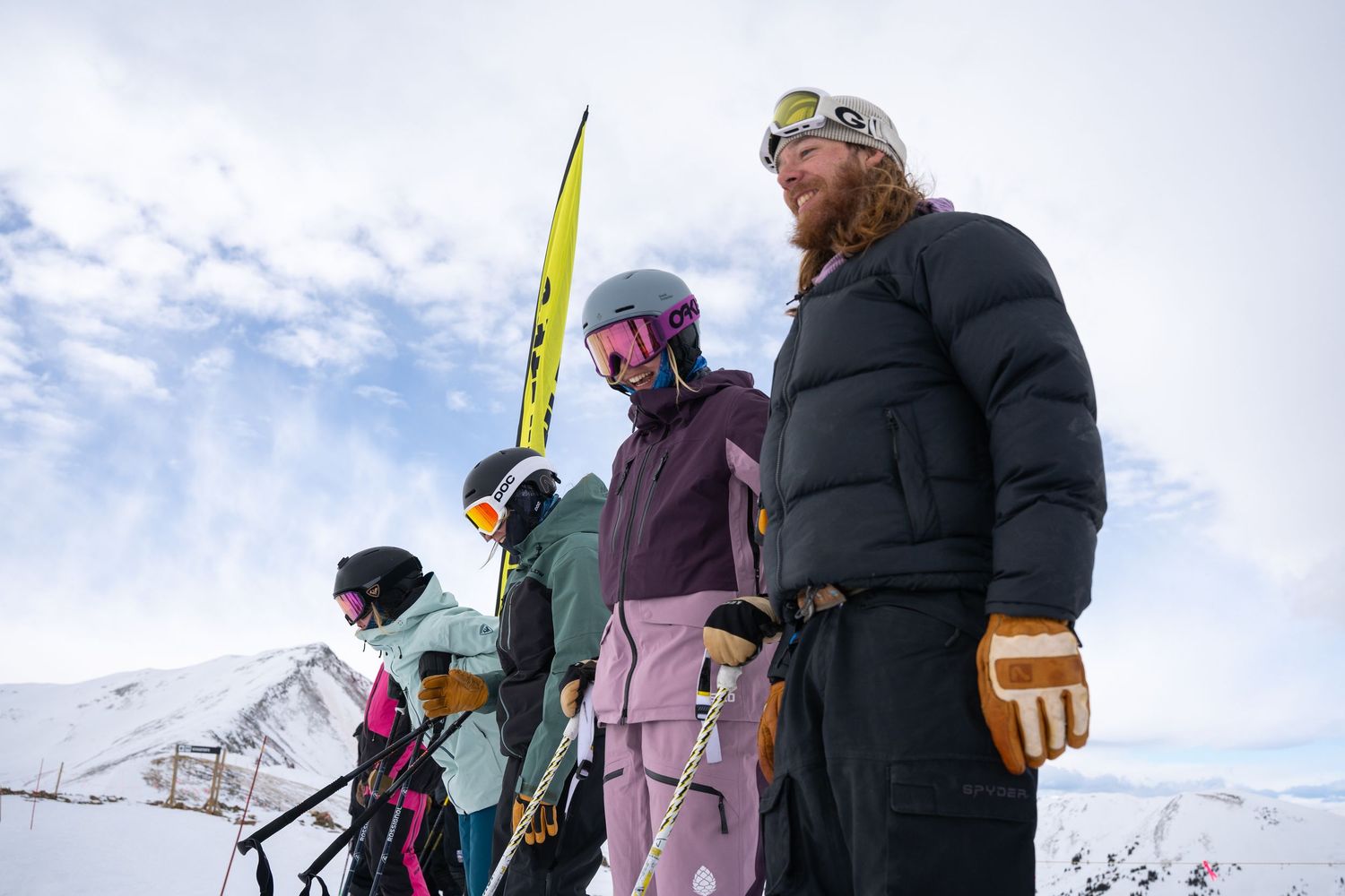 Group of winter sports enthusiasts stand together on snowy mountain terrain.
