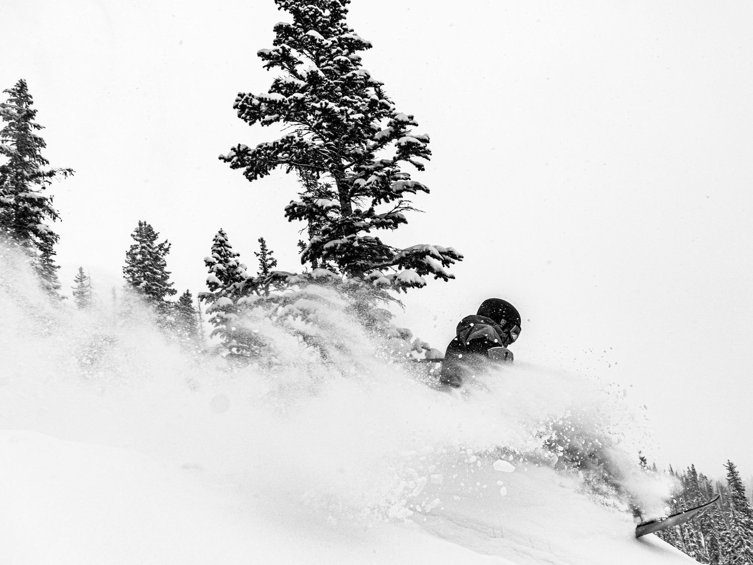 Snowboarder carving through deep powder snow in black and white winter scene.