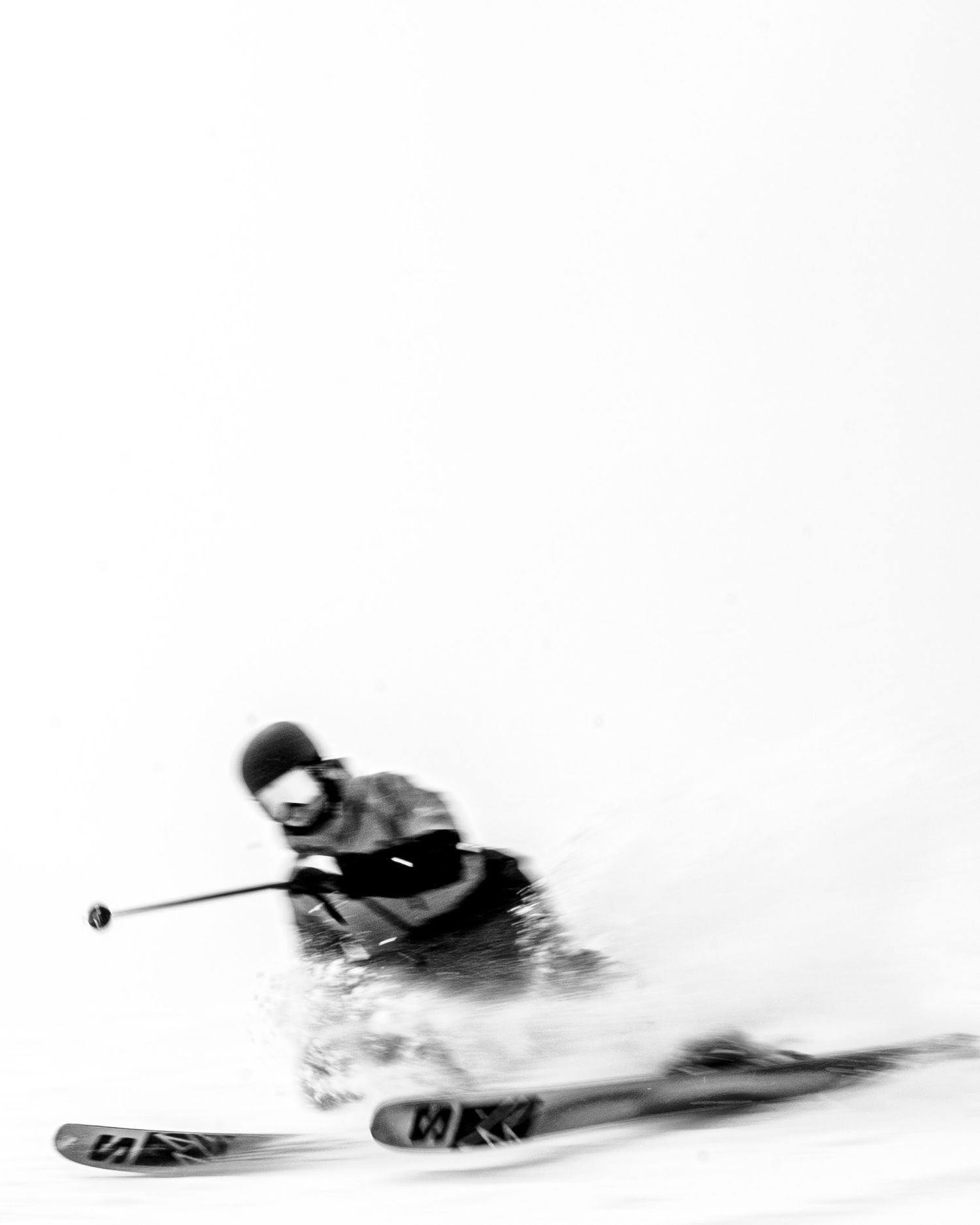 Motion blur black and white image of downhill skier carving through powder snow.