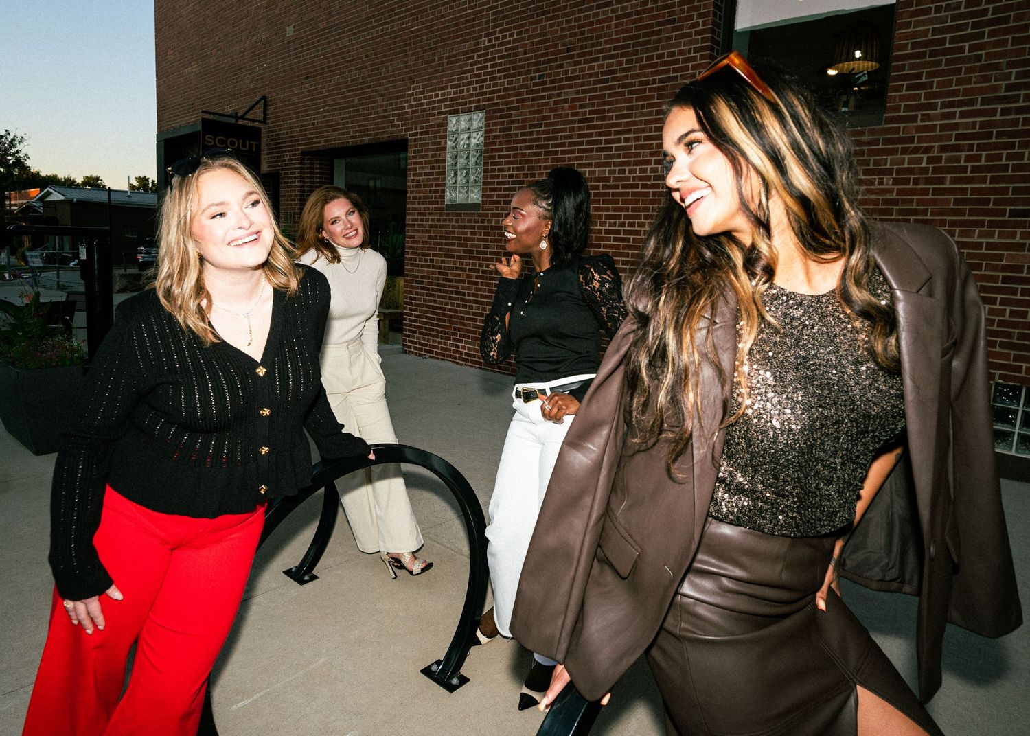 A group of people gather and socialize at a casual nighttime event outside a brick building.