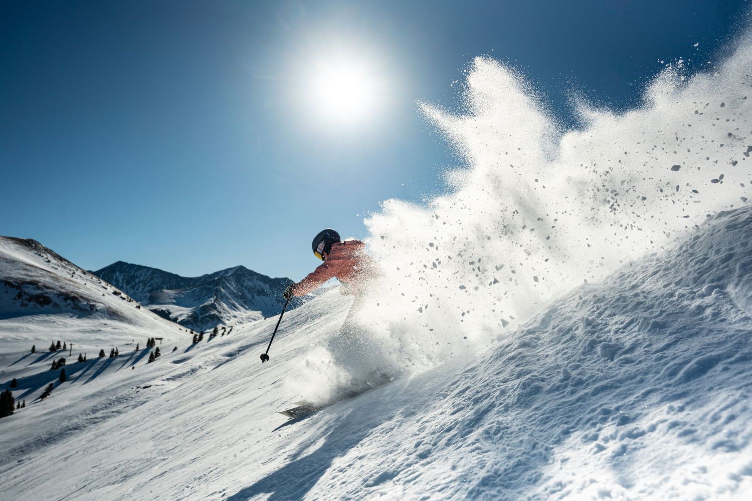 Skier spraying powder snow while making a dramatic turn on a sunny mountain slope.