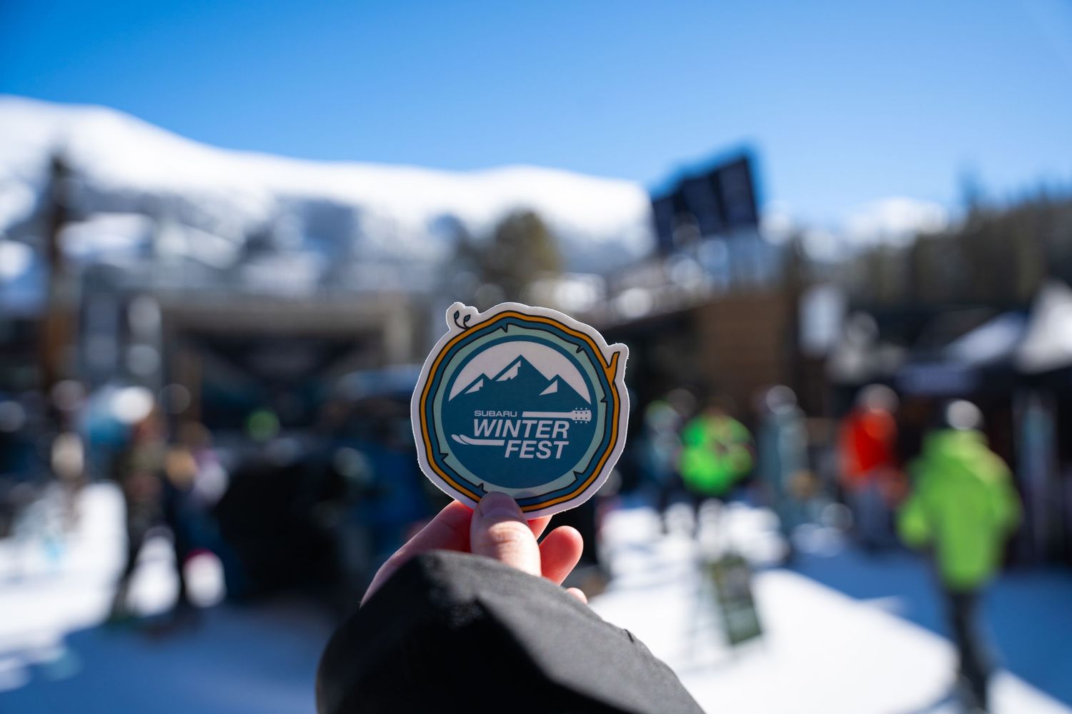 Hand holding WinterFest event medallion against snowy mountain background.