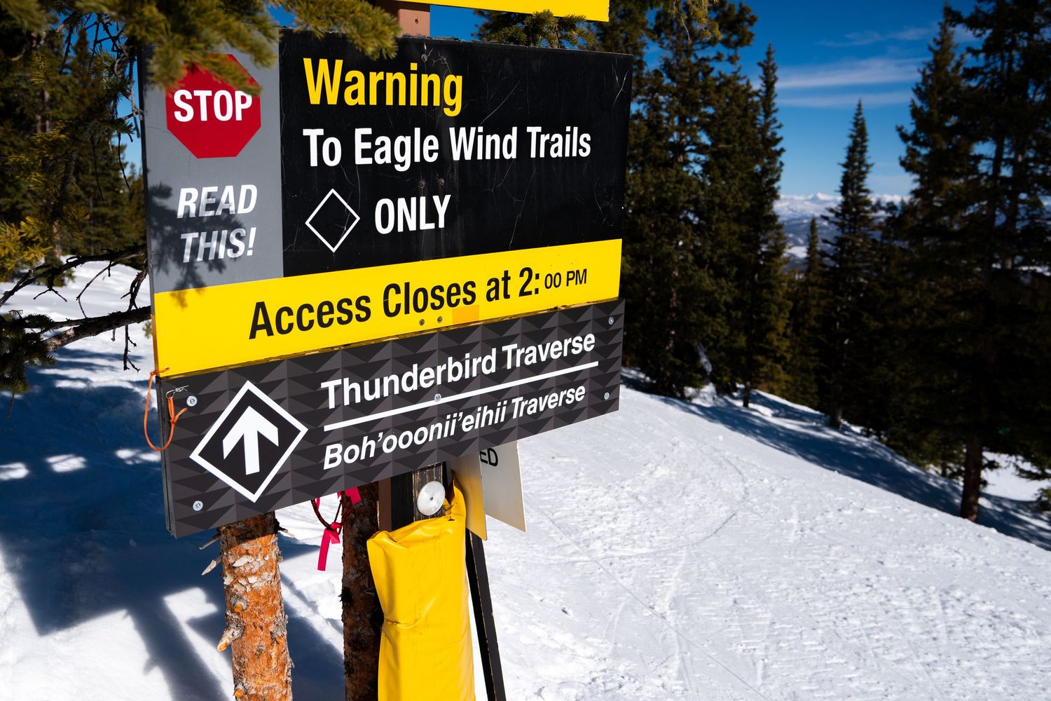 Warning sign for Eagle Wind Trails ski run with stop sign and distance markers in snowy mountain setting.
