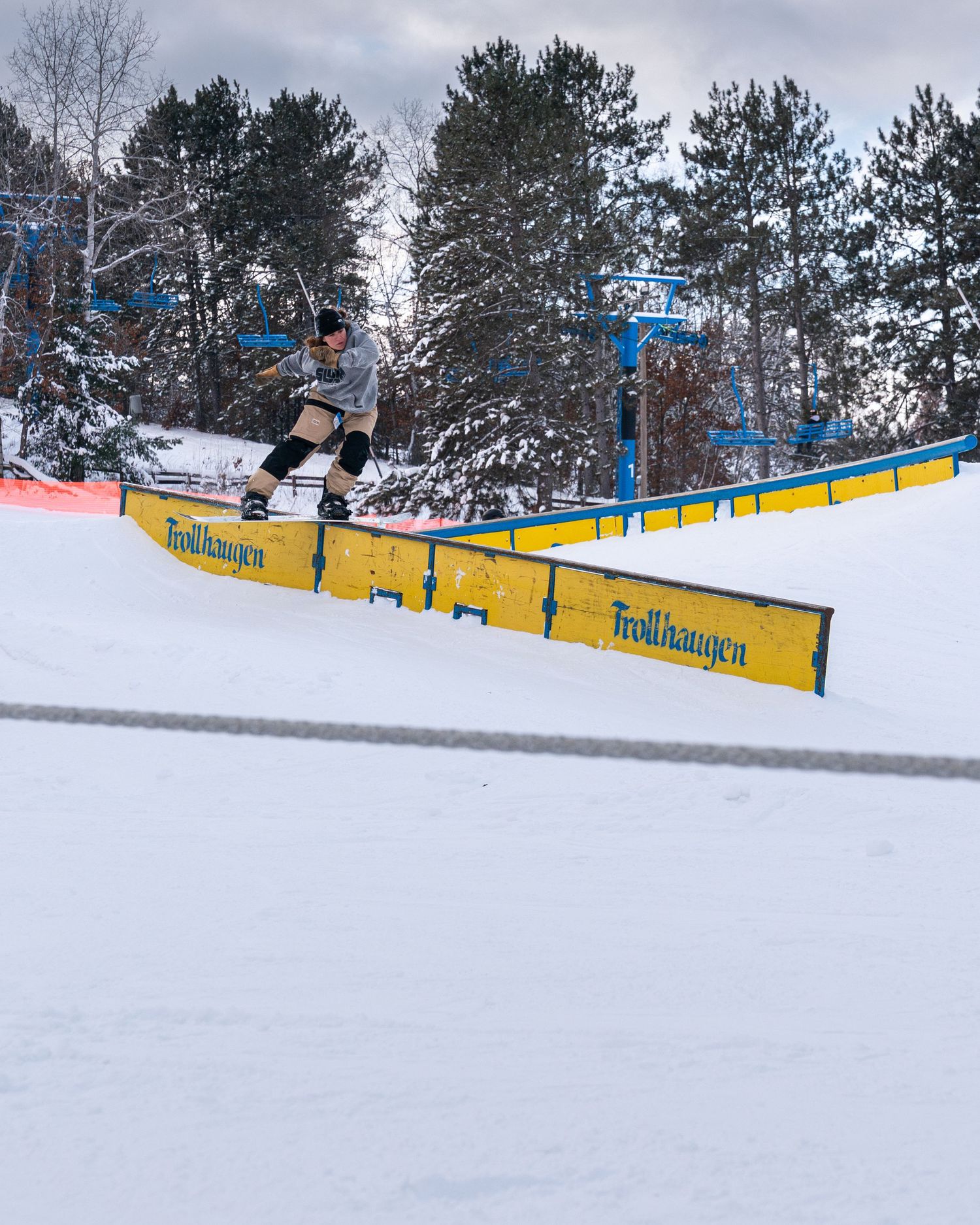 Snowboarder grinding a yellow rail at Trollhaugen ski resort surrounded by snow-covered trees.
