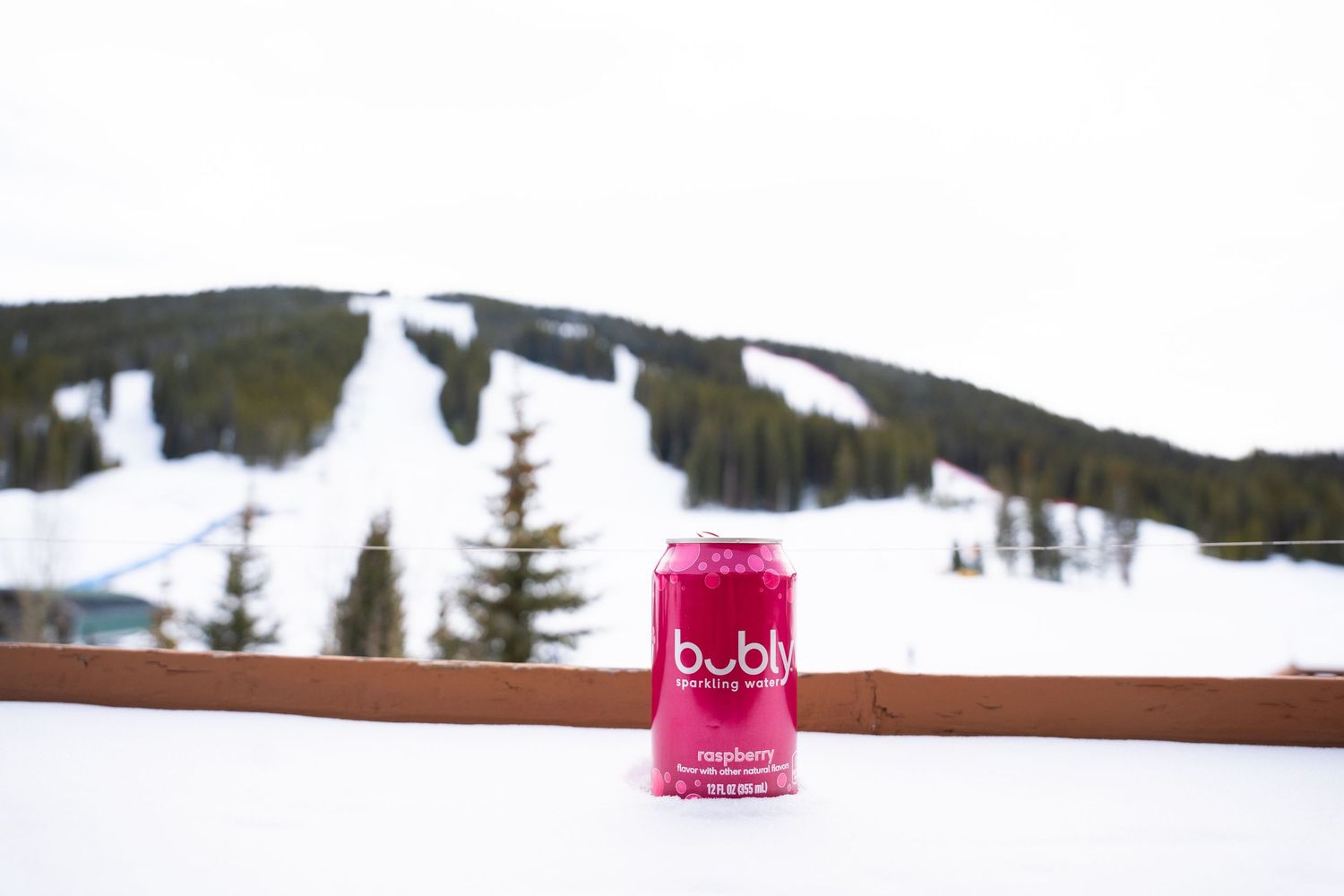 Pink Bubly can sitting on wooden railing with snow-covered ski slopes in background.