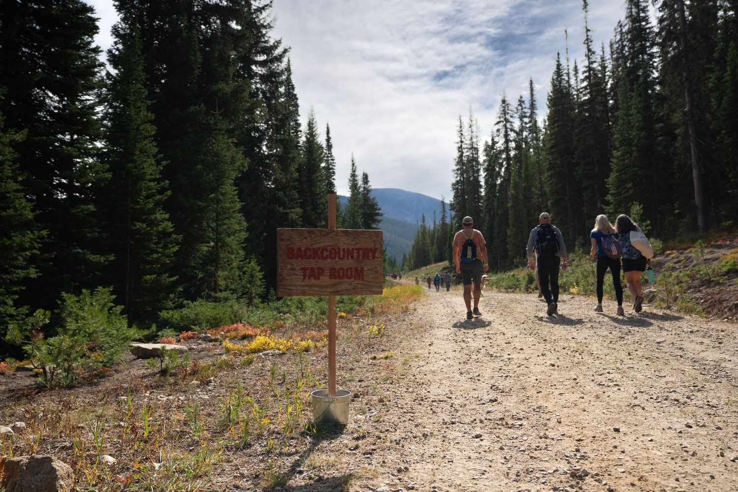 Hiking group walking on mountain trail with warning sign and evergreen forest.