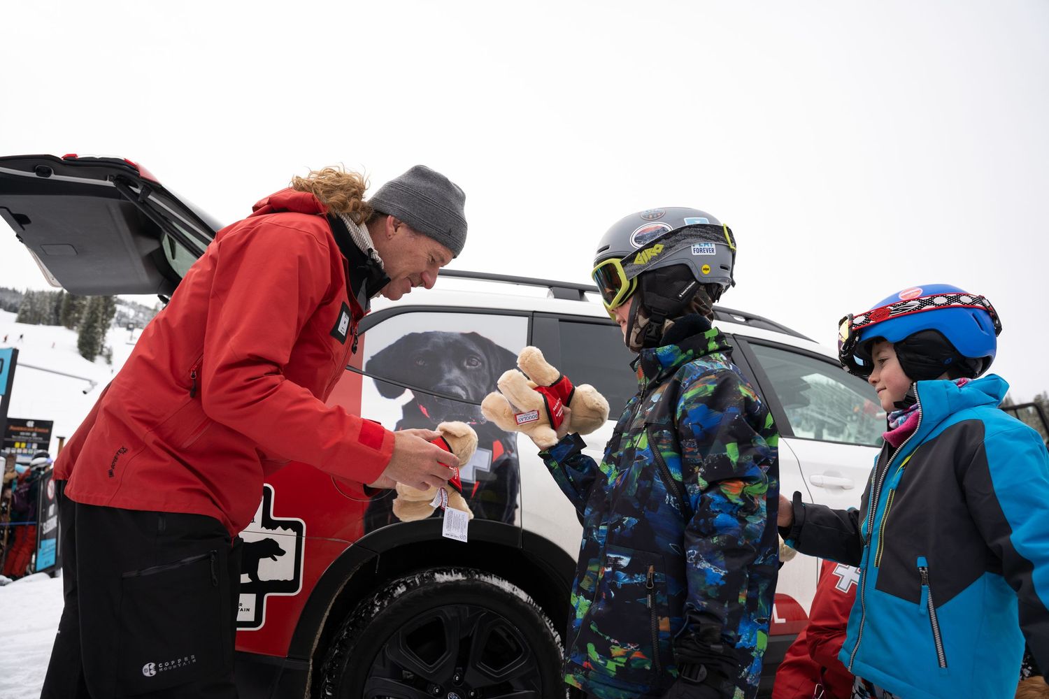 People gathering around a vehicle in a snowy parking lot during a winter sports event.