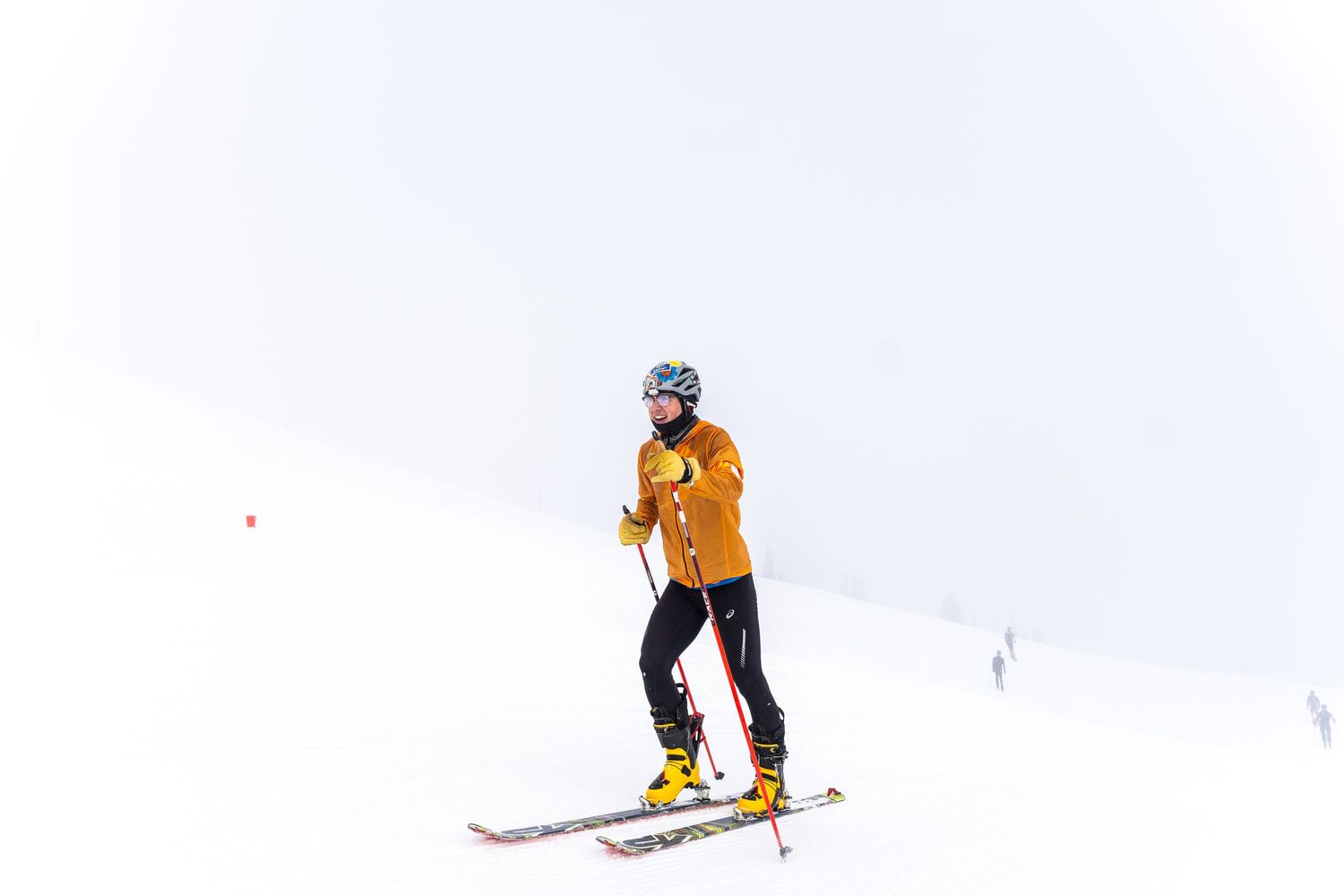 Skier in bright orange jacket makes their way down a snow-covered slope.