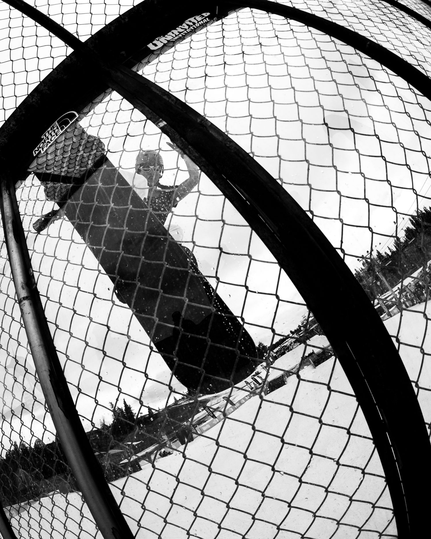 Black and white photo of a person's shadow reflected on a chain-link fence in a snowy winter landscape.
