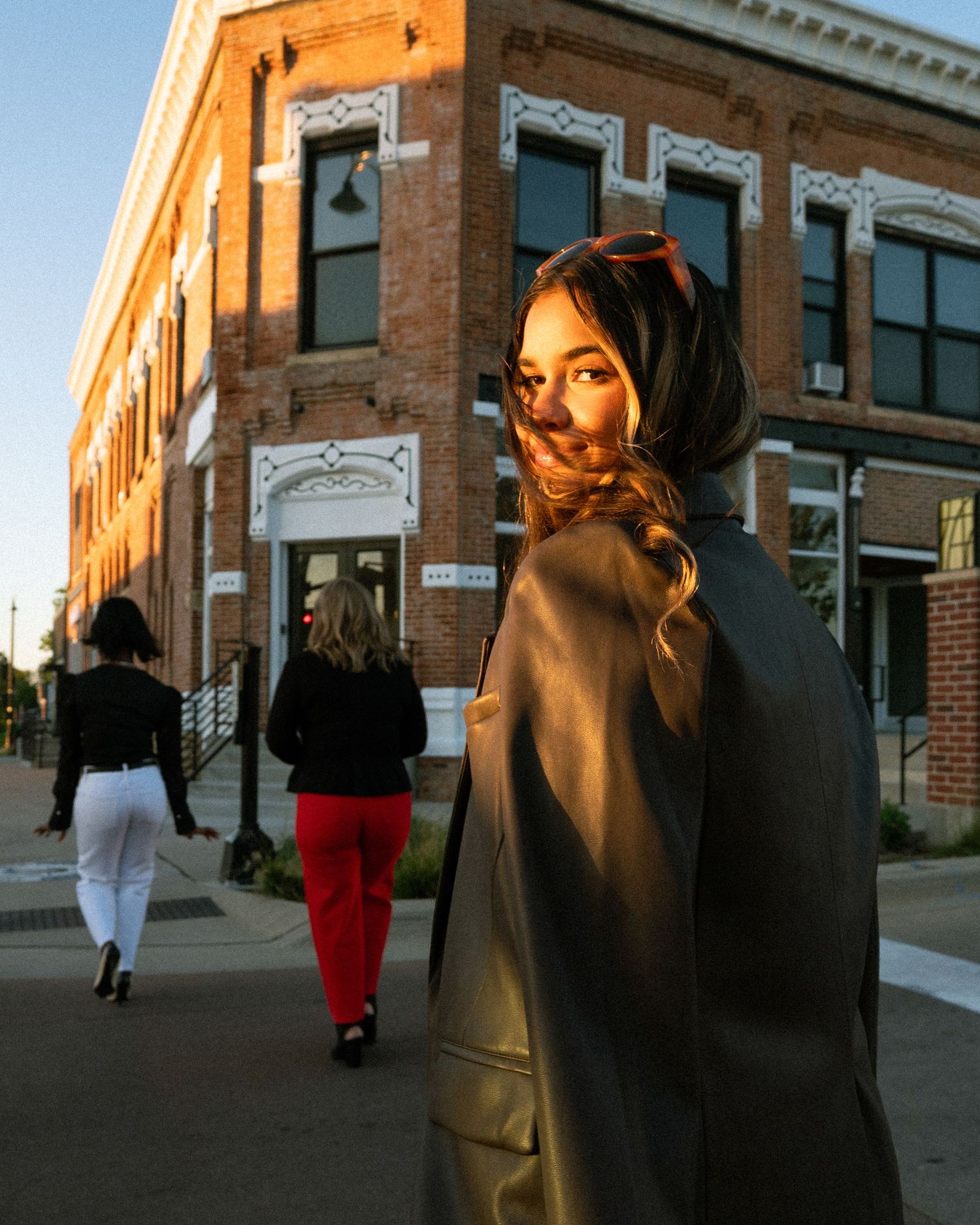 People walking along brick storefronts during golden hour casting long shadows.